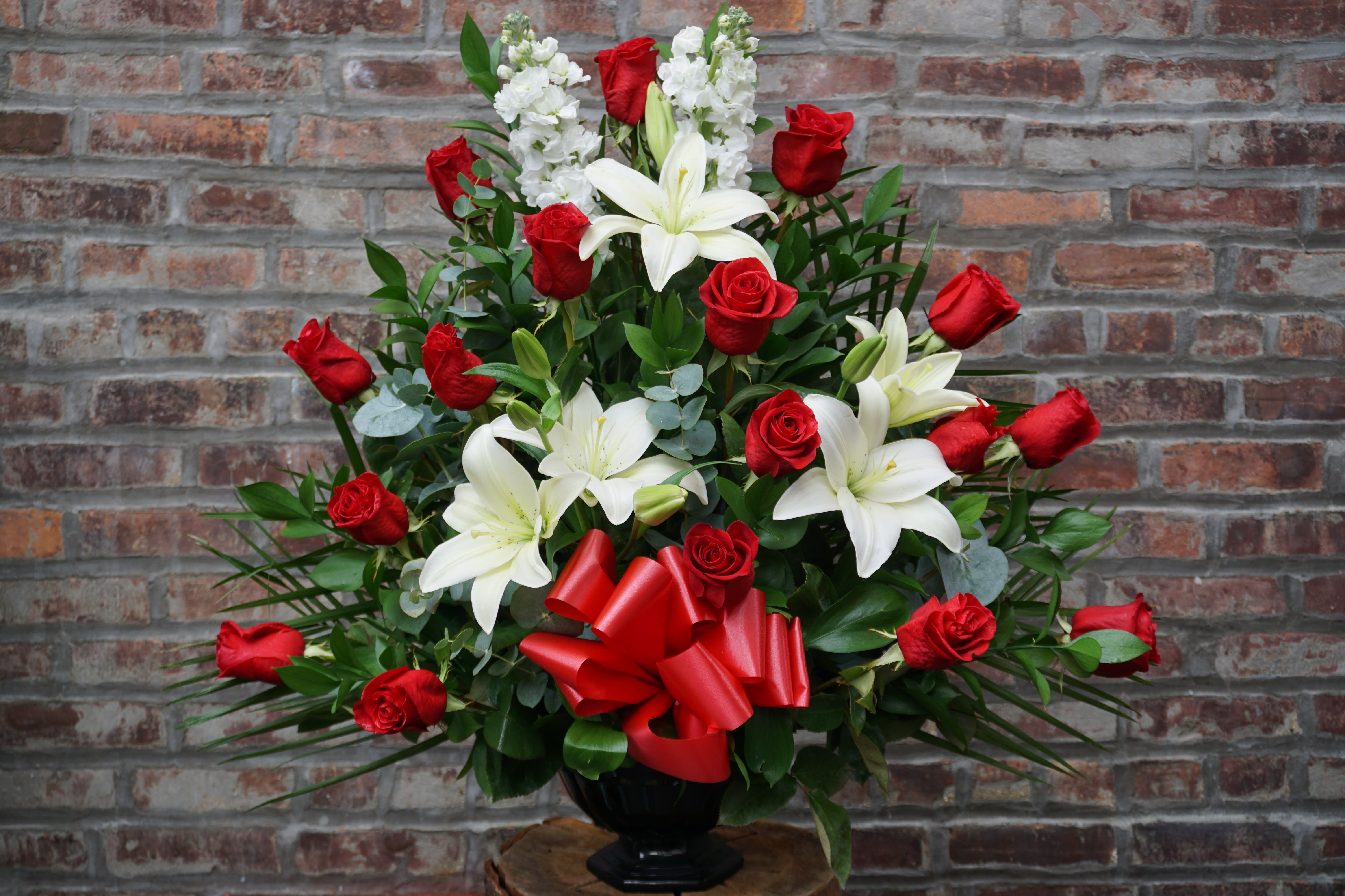 Red roses and white lilies in a black vase with a red bow