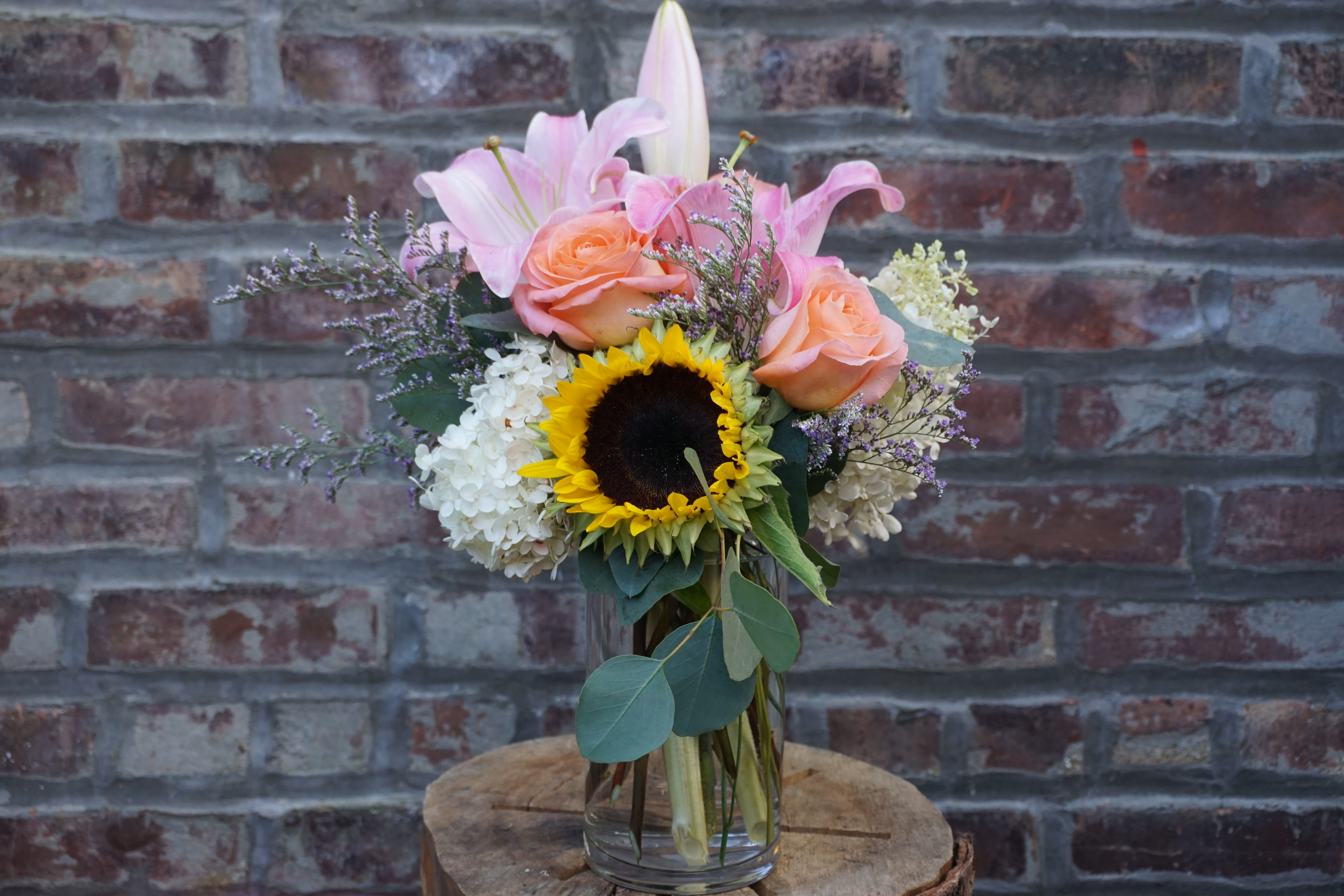 Bouquet of pink lilies, peach roses, and a sunflower in a glass vase