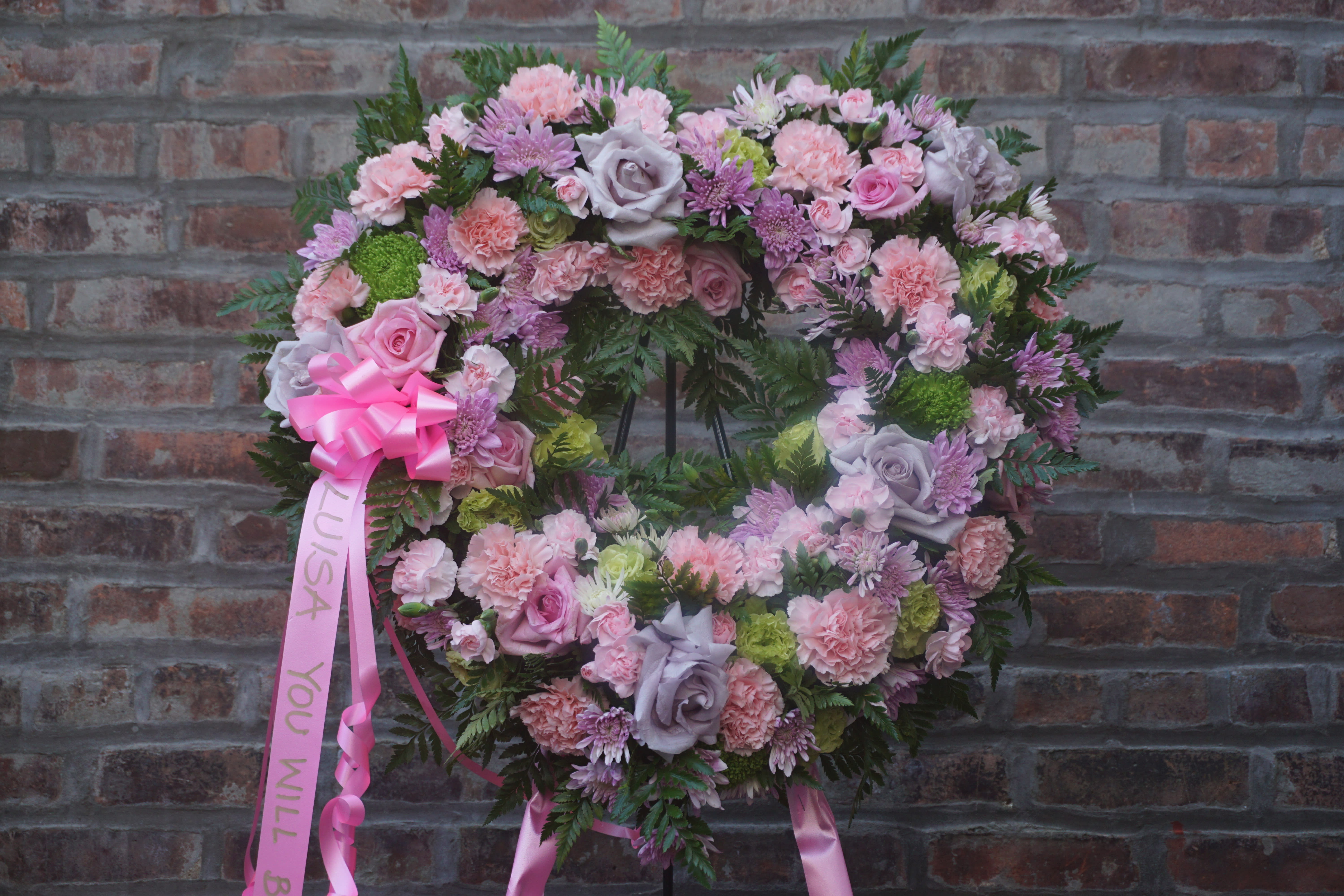 Heart-shaped floral wreath with pink and lavender flowers on a brick wall