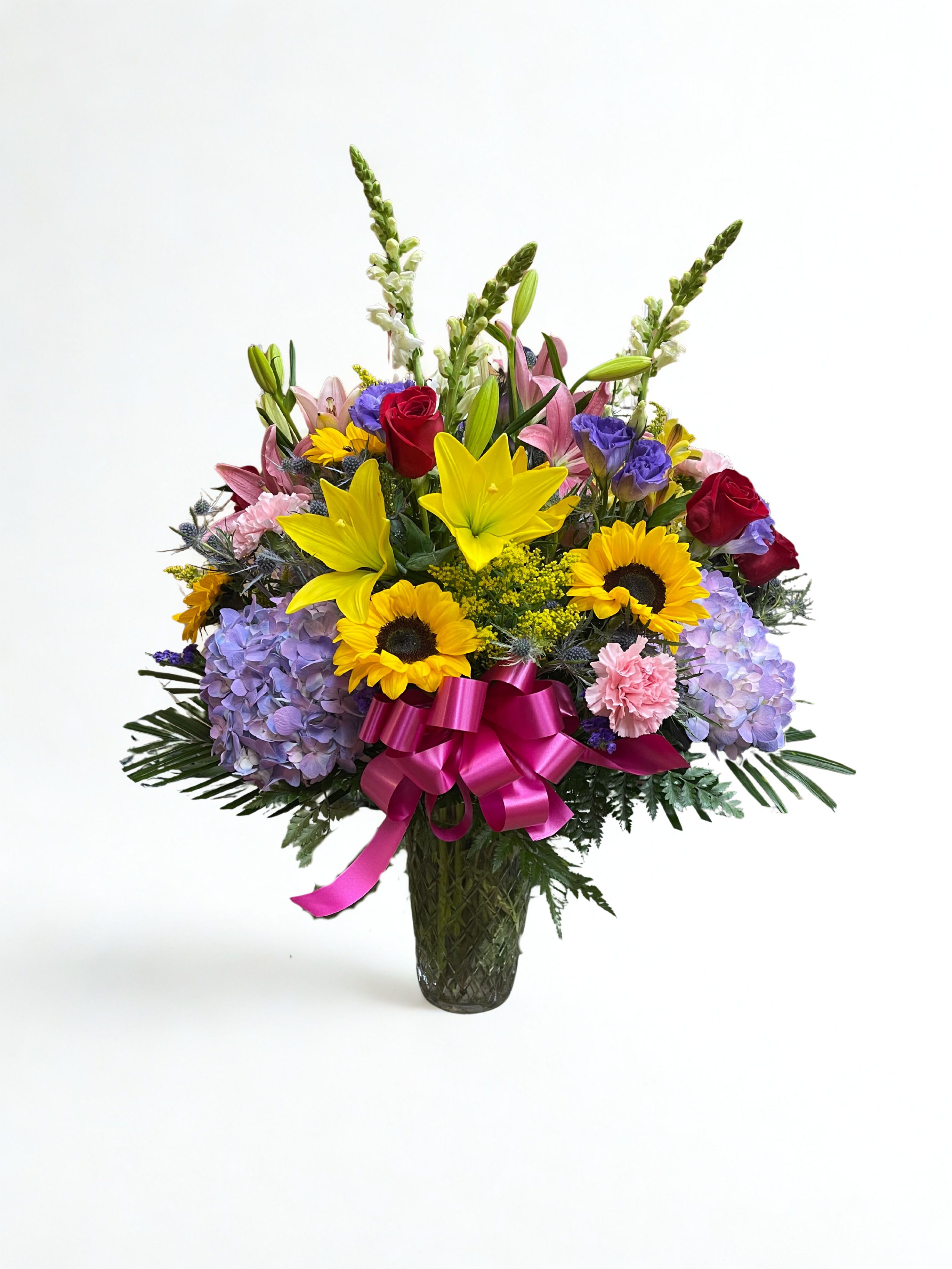 Mixed bouquet of lilies, roses, sunflowers, and hydrangeas in a glass vase