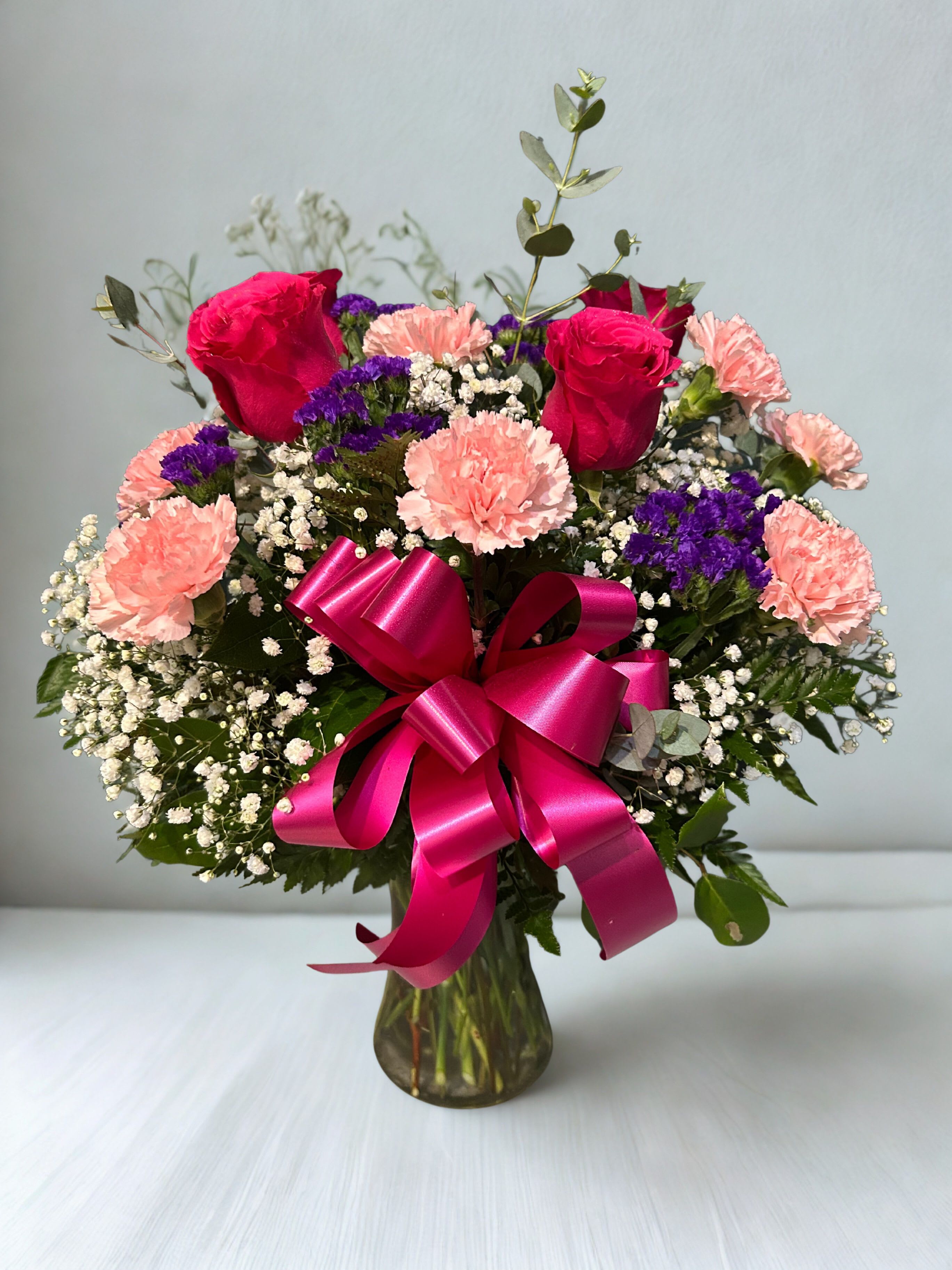 Bouquet of pink roses and carnations with purple filler in a glass vase