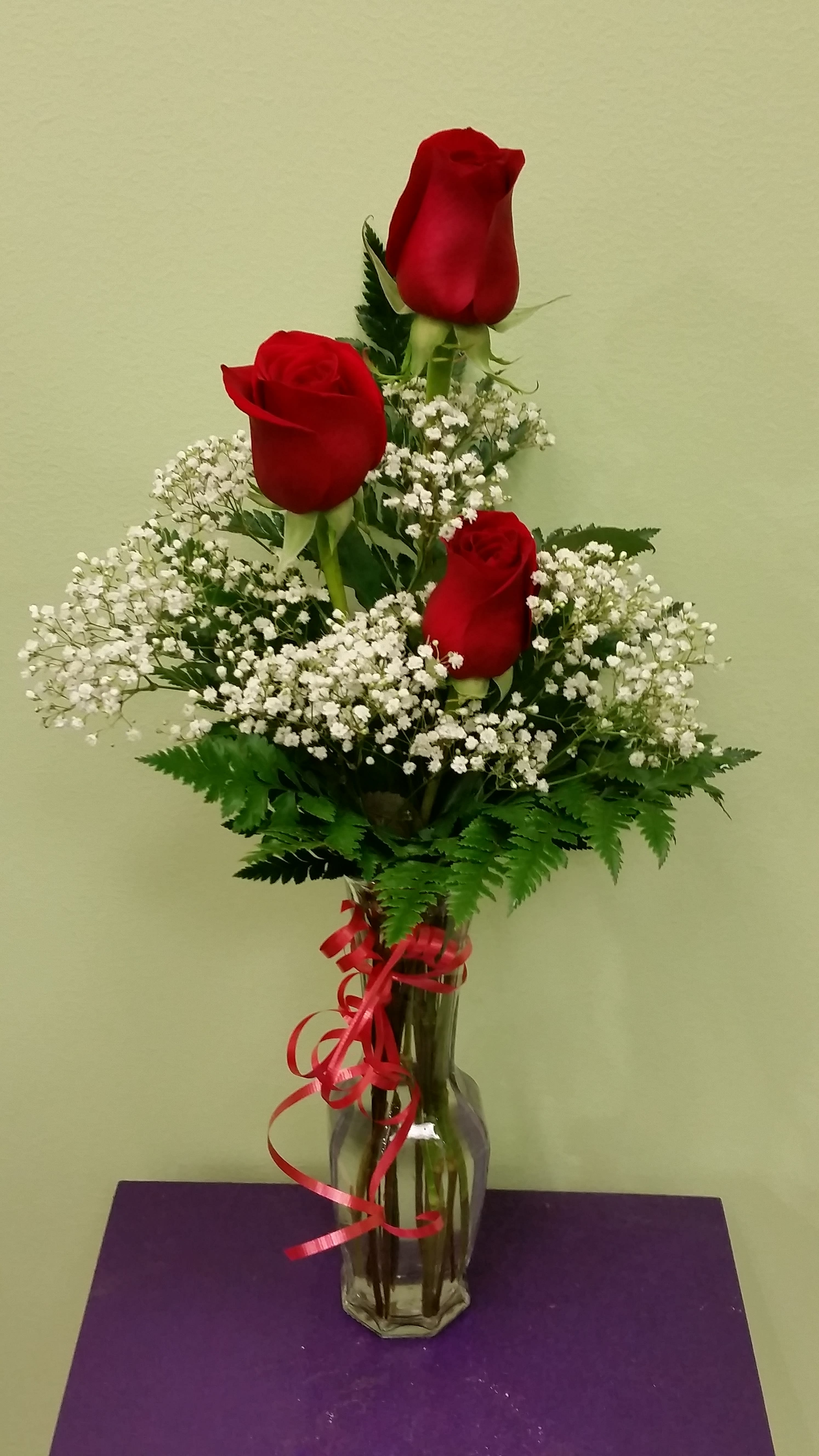 Three red roses in a clear glass vase with white baby's breath
