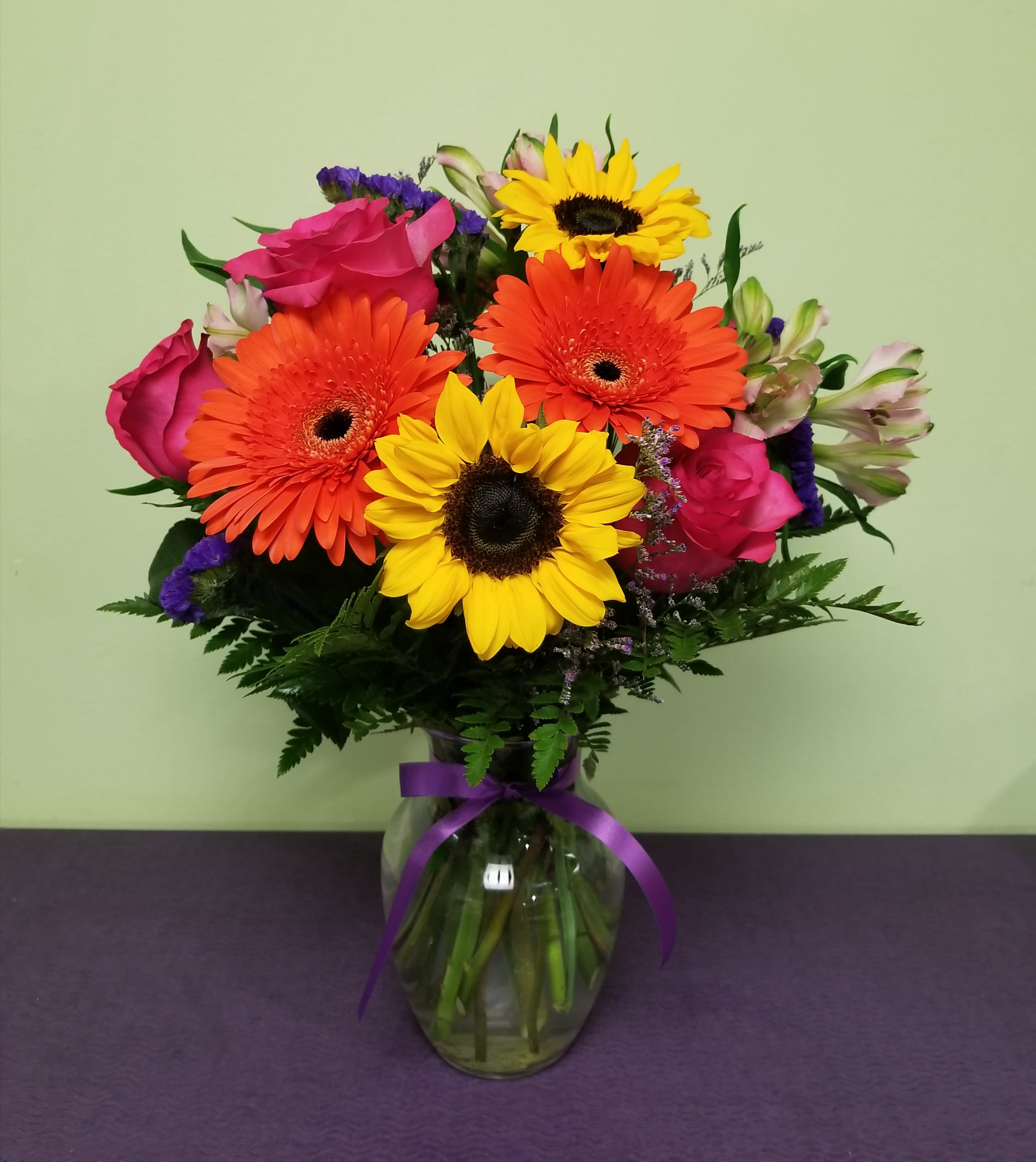 Bouquet of sunflowers, gerbera daisies, and pink roses in a glass vase