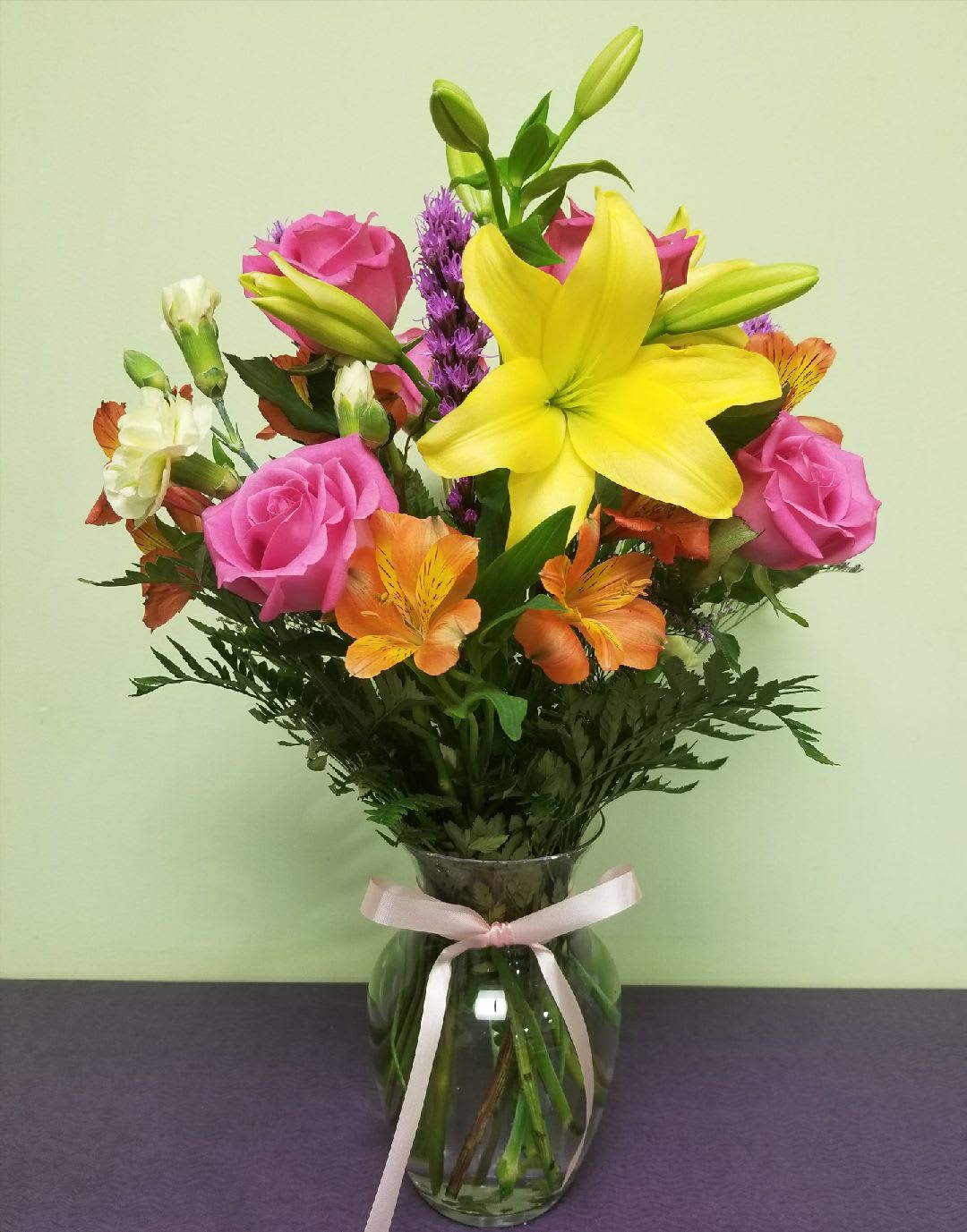 Bouquet of pink roses, yellow lilies, and orange alstroemeria in a glass vase