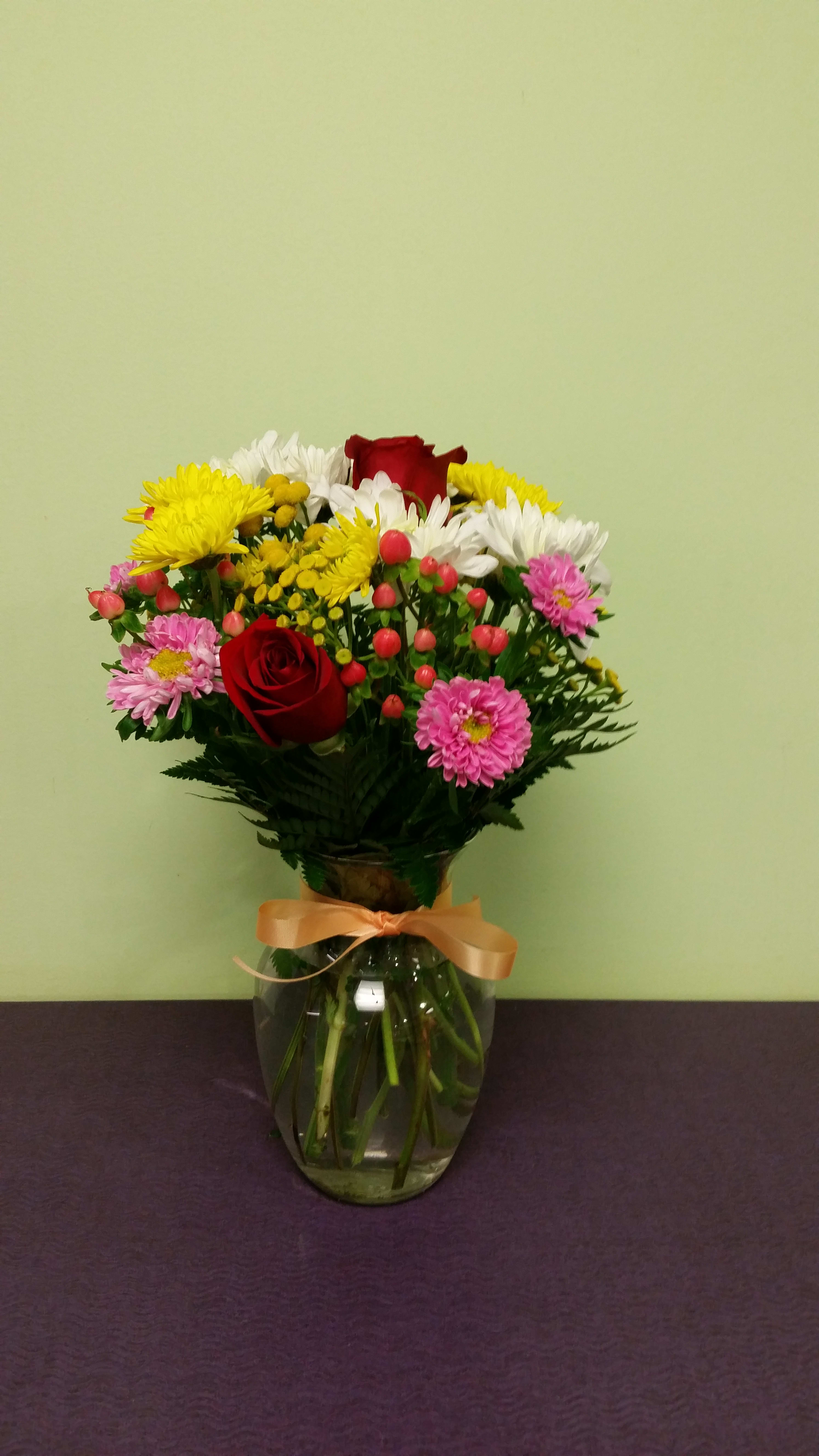 Mixed bouquet of roses and daisies in a glass vase with a ribbon