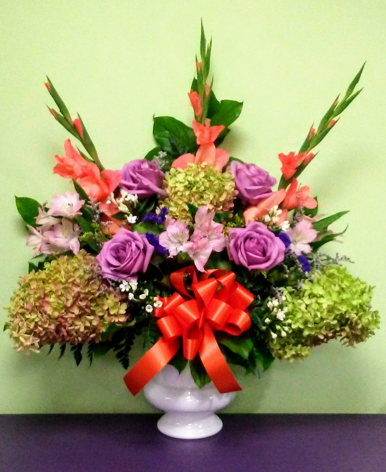 Colorful mixed flower arrangement in a white vase with a red bow