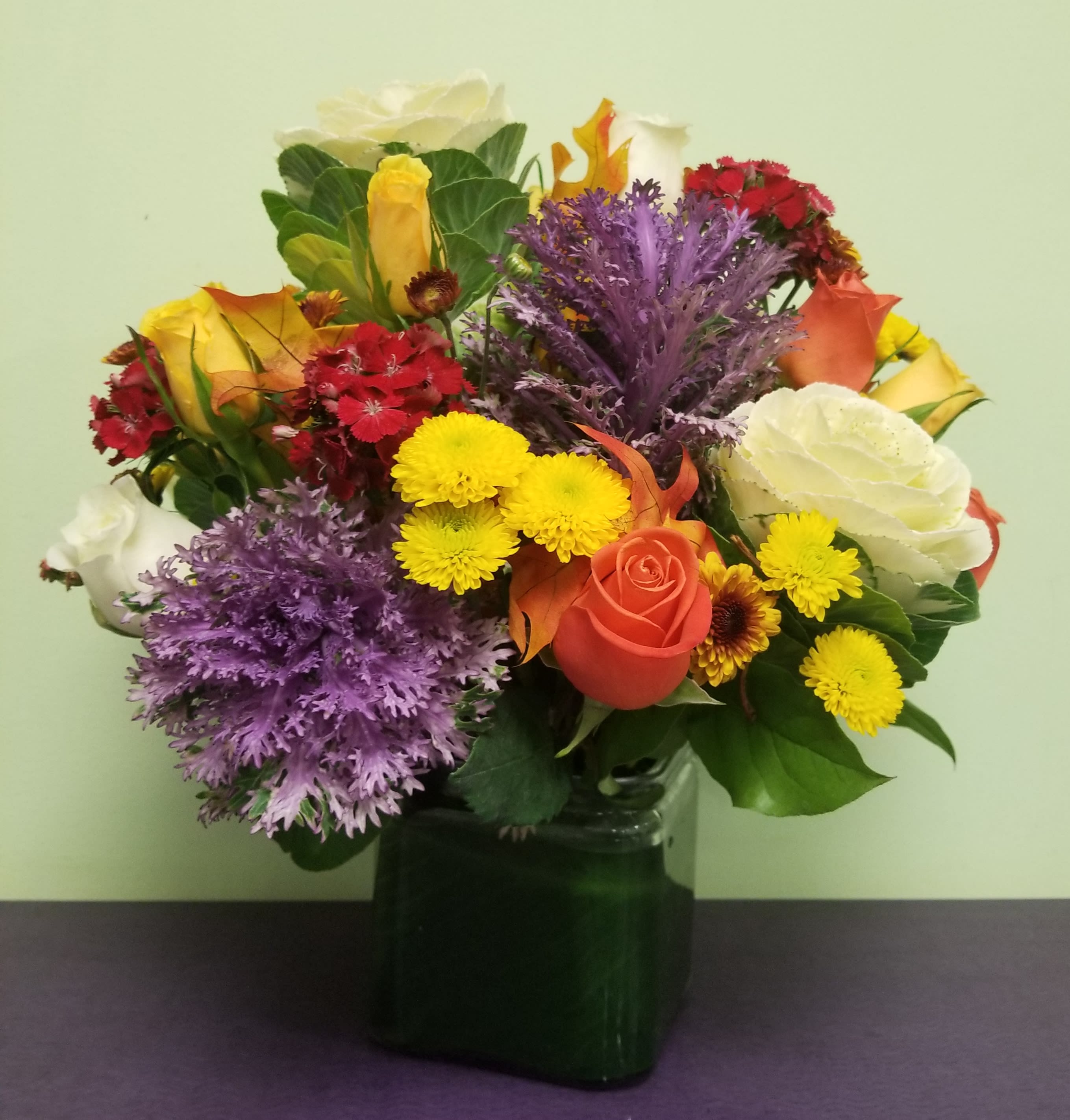 Mixed bouquet of roses, chrysanthemums, and carnations in a dark glass vase