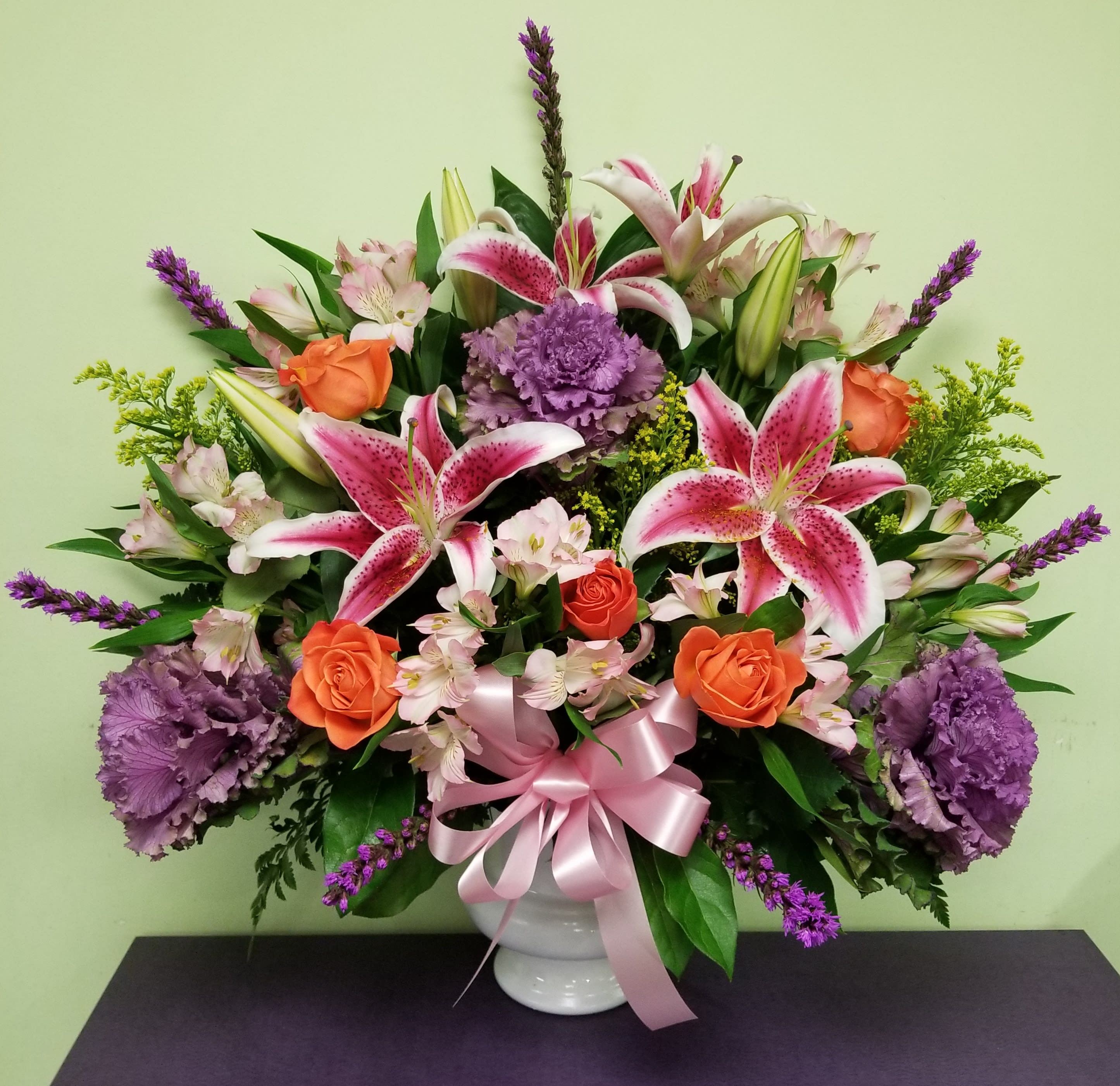 Bouquet of pink lilies, orange roses, and purple flowers in a white vase