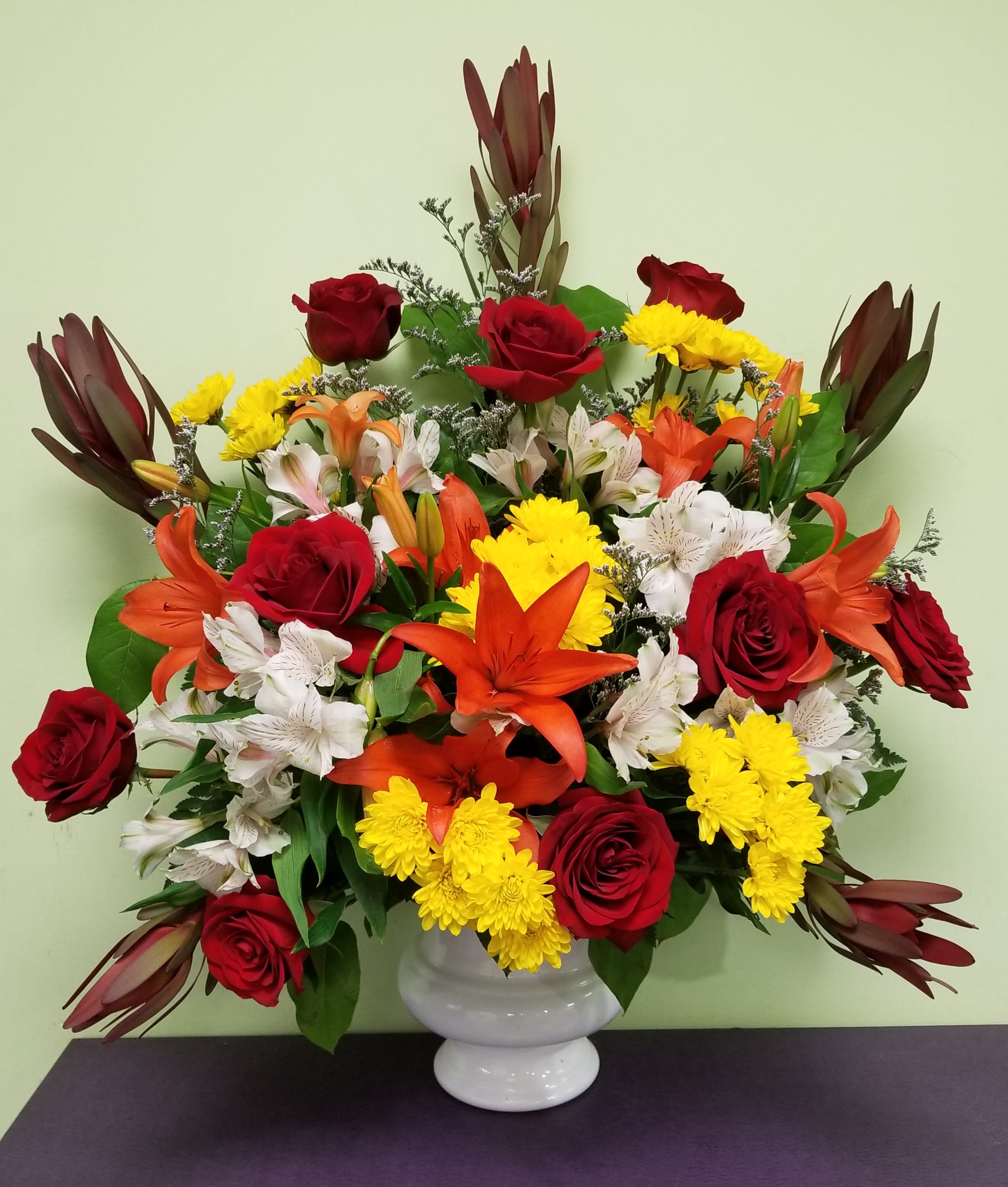 Mixed bouquet of red roses, orange lilies, and yellow chrysanthemums in a white vase