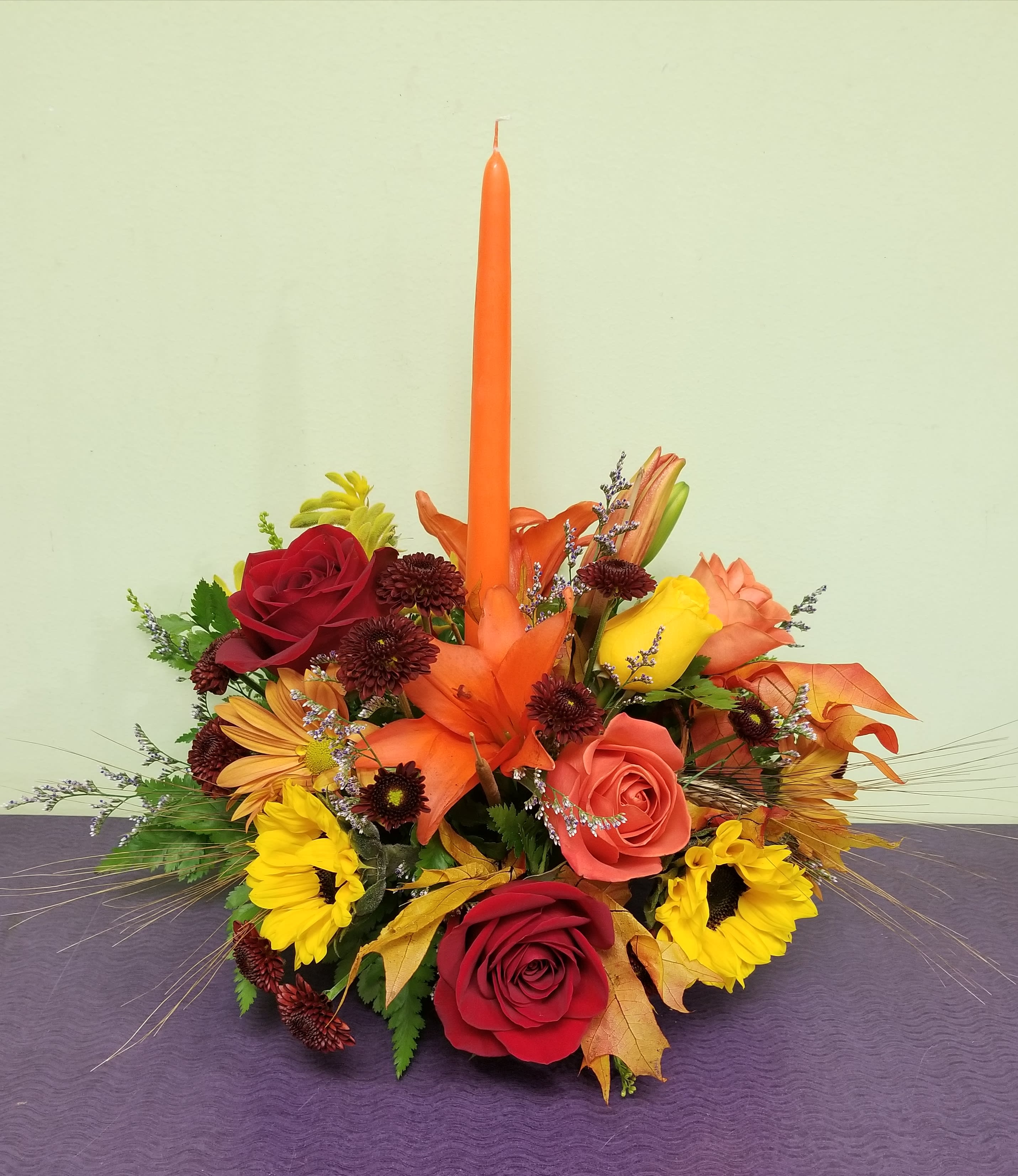 Autumn floral centerpiece with roses, sunflowers, and a tall orange taper candle