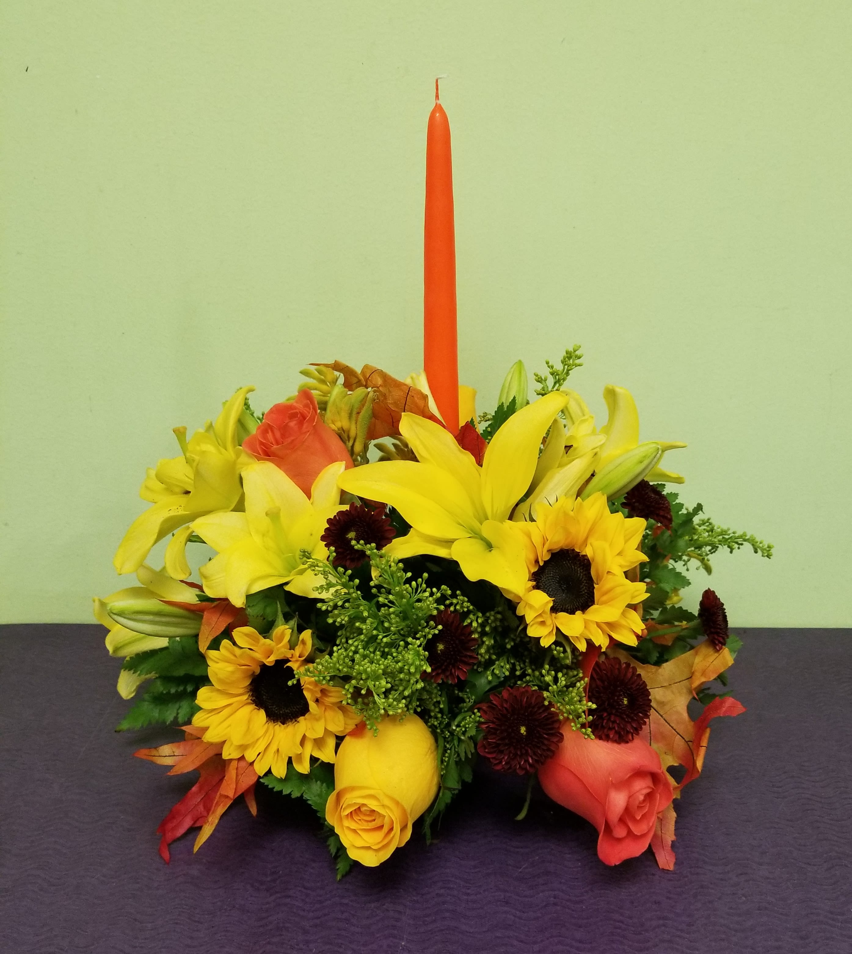 Yellow lilies and sunflowers arranged around a tall orange candle