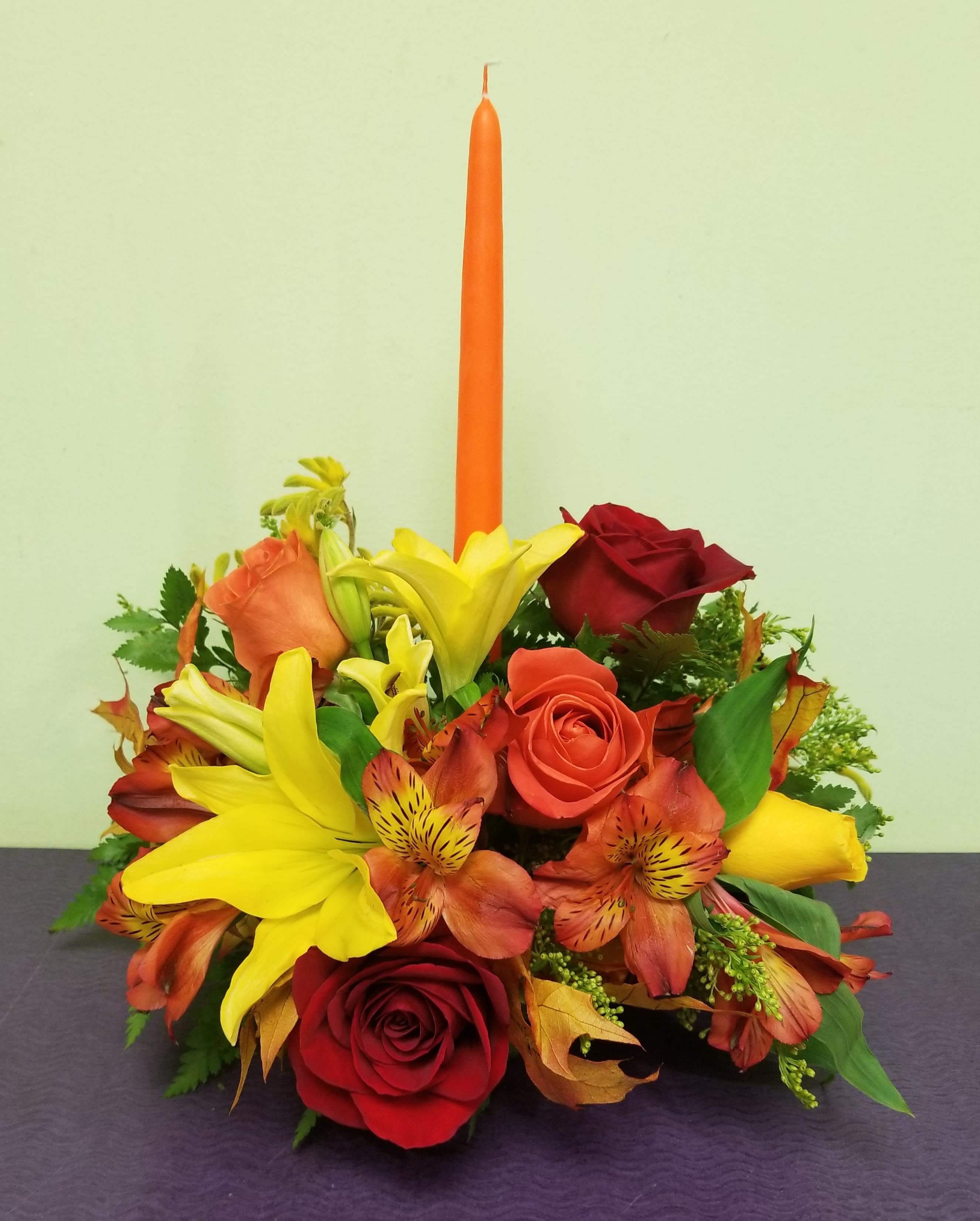 Red and yellow floral arrangement with a tall orange candle