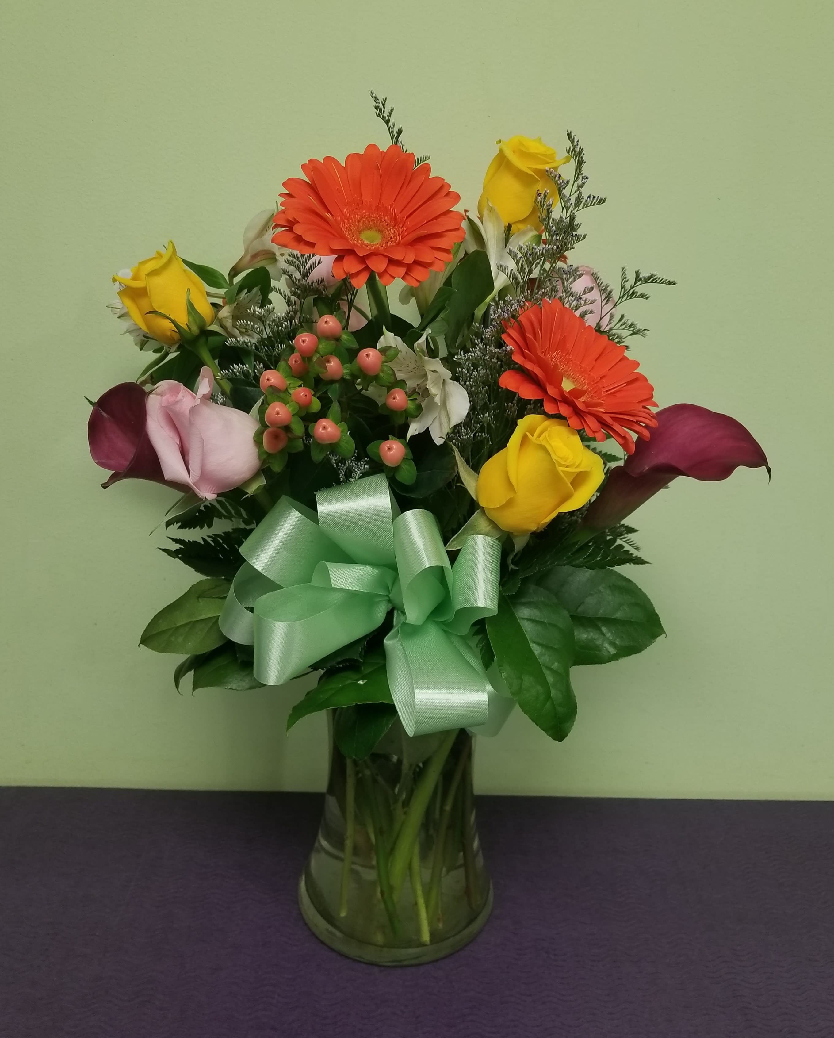 Bouquet of yellow roses, orange gerberas, and purple calla lilies in a glass vase