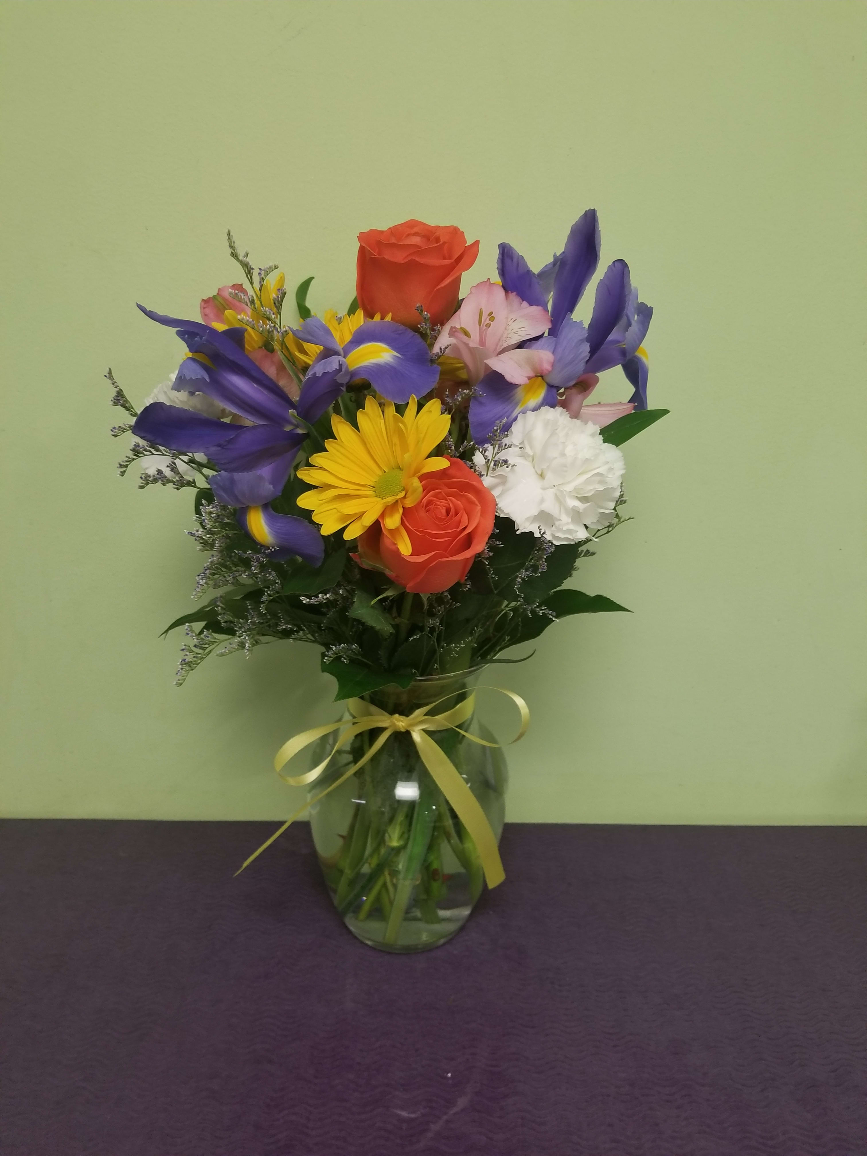 Mixed bouquet of roses, irises, daisies, and carnations in a glass vase