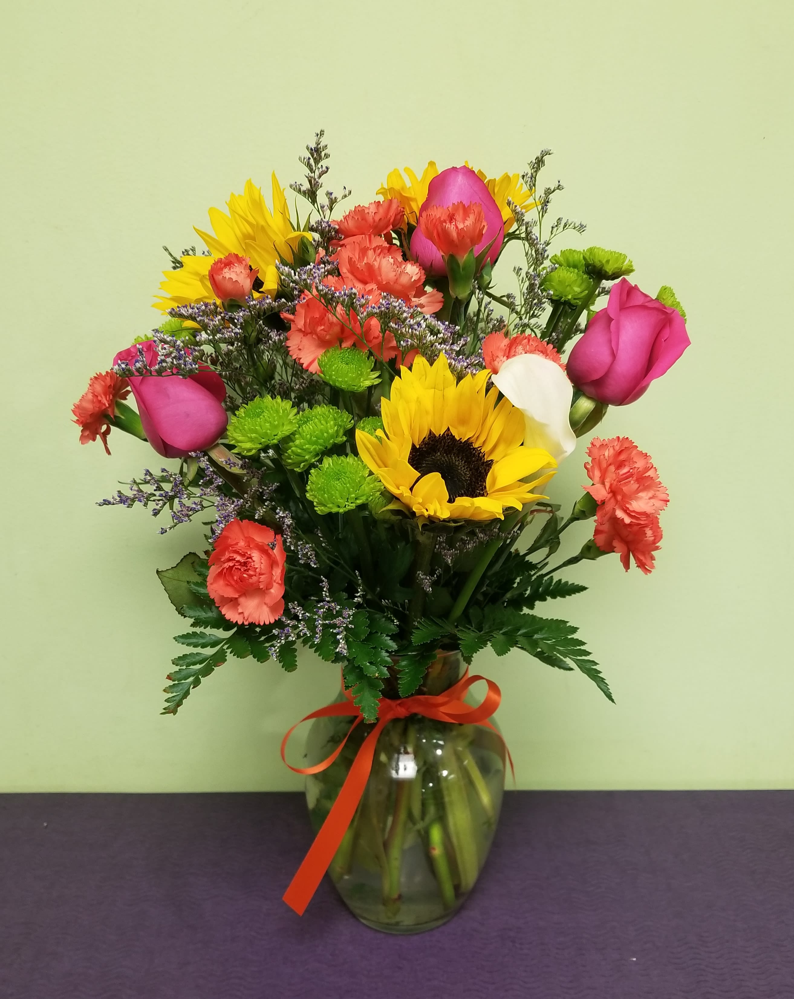 Mixed bouquet with sunflowers, pink roses, carnations, and a glass vase