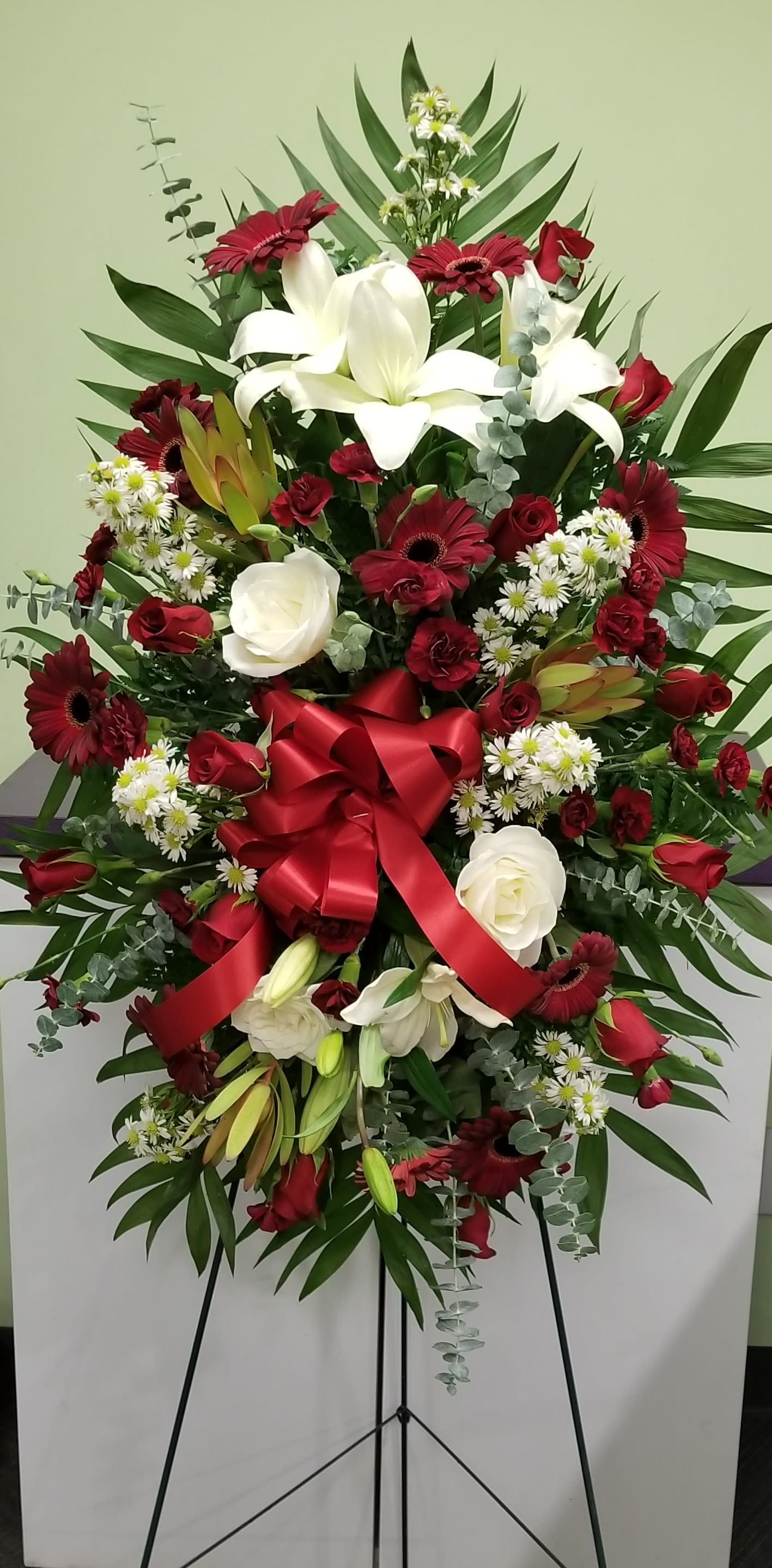 Large standing floral spray with red and white flowers and a red ribbon bow