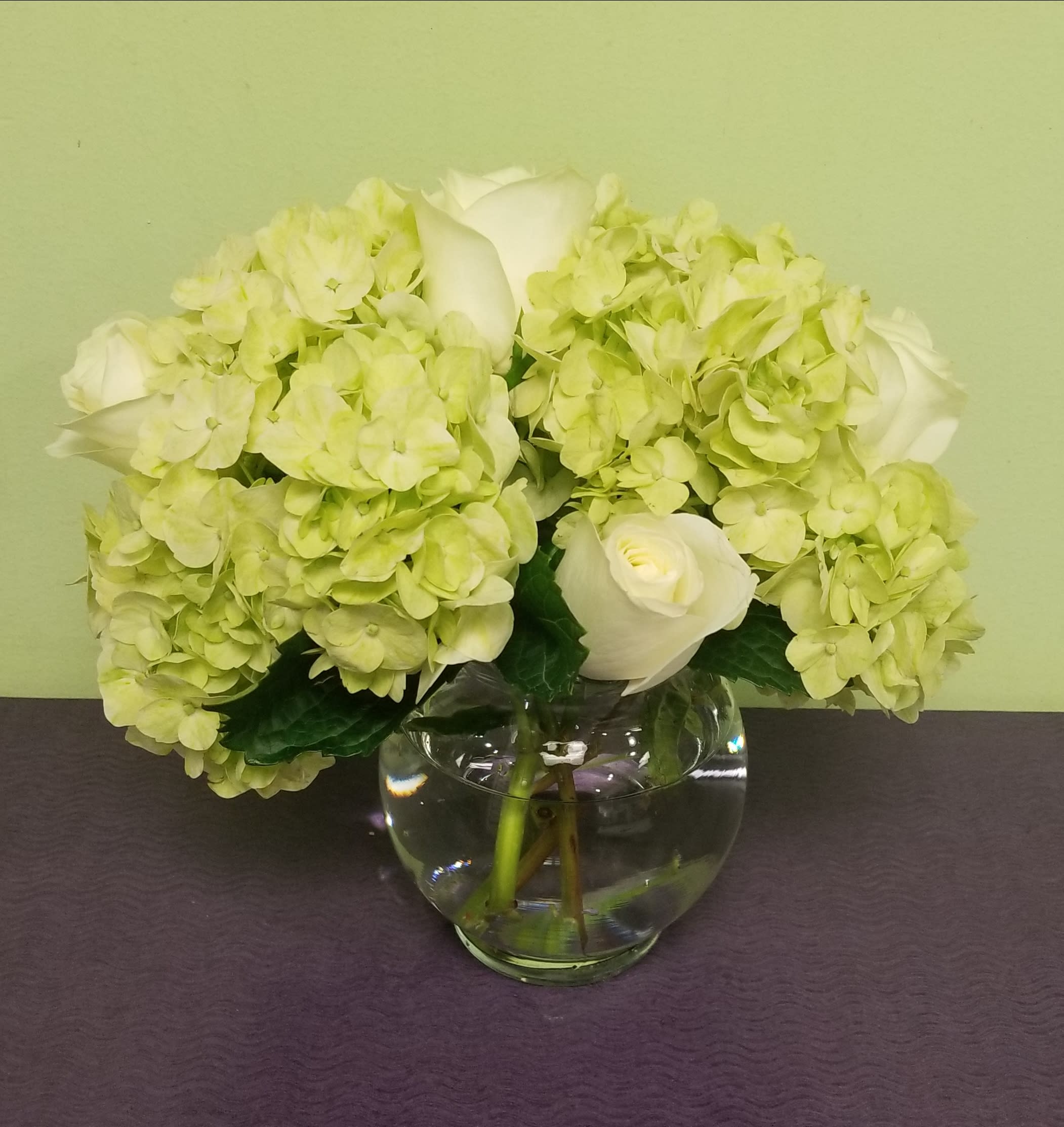 White roses and pale green hydrangeas in a clear glass vase