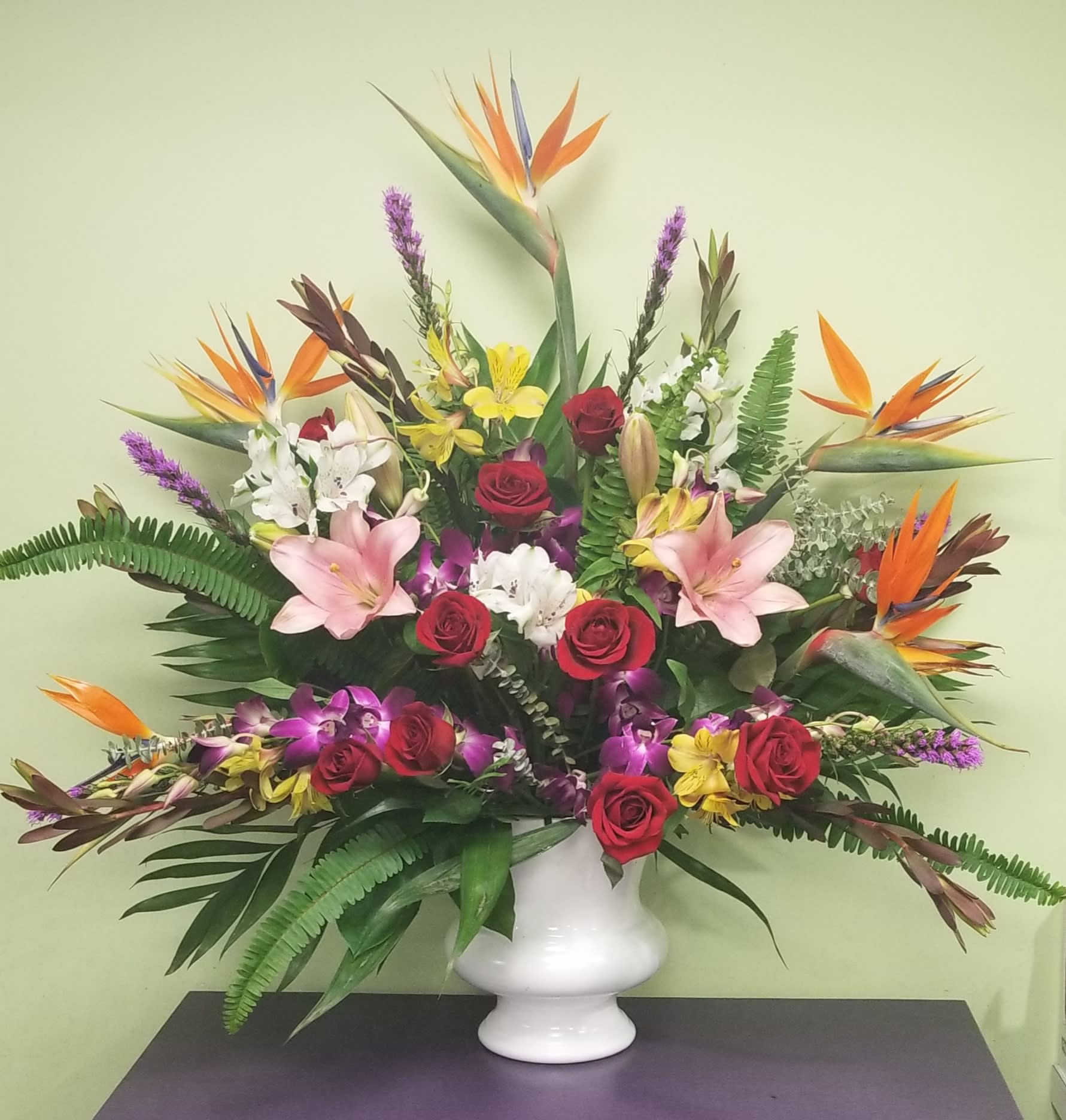 Tropical flower arrangement with roses, lilies, and bird-of-paradise in a white vase