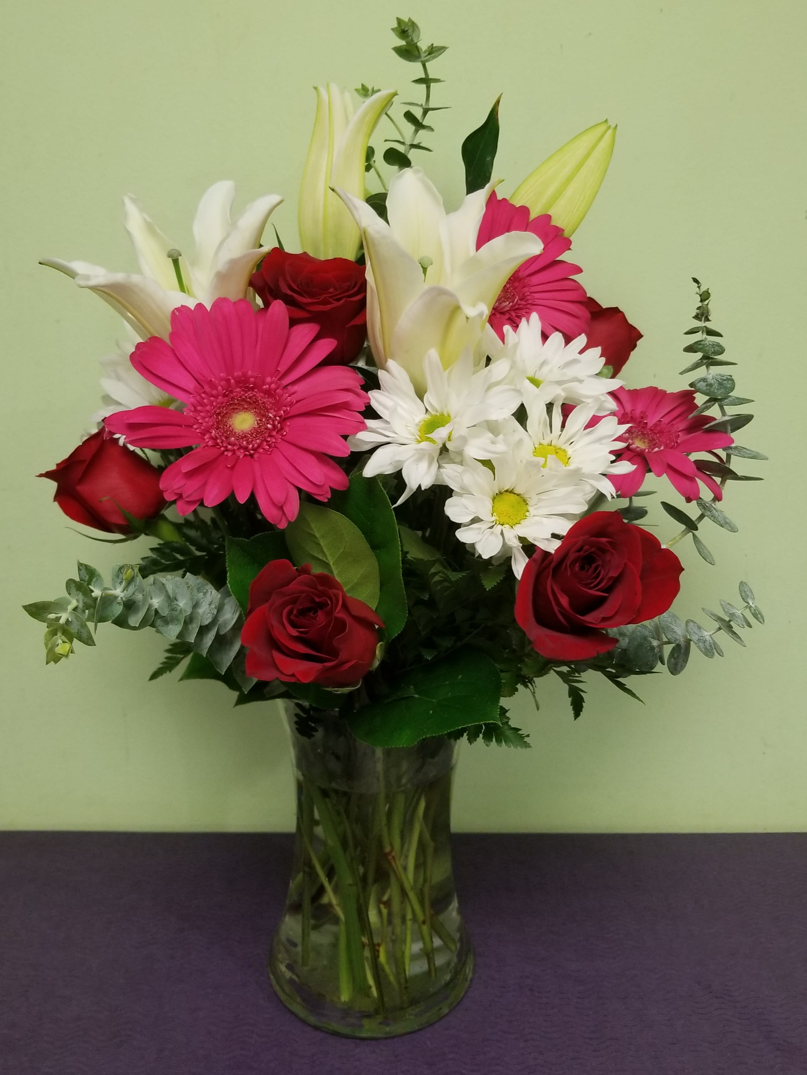 Bouquet of red roses, pink gerberas, white lilies, and daisies in a glass vase