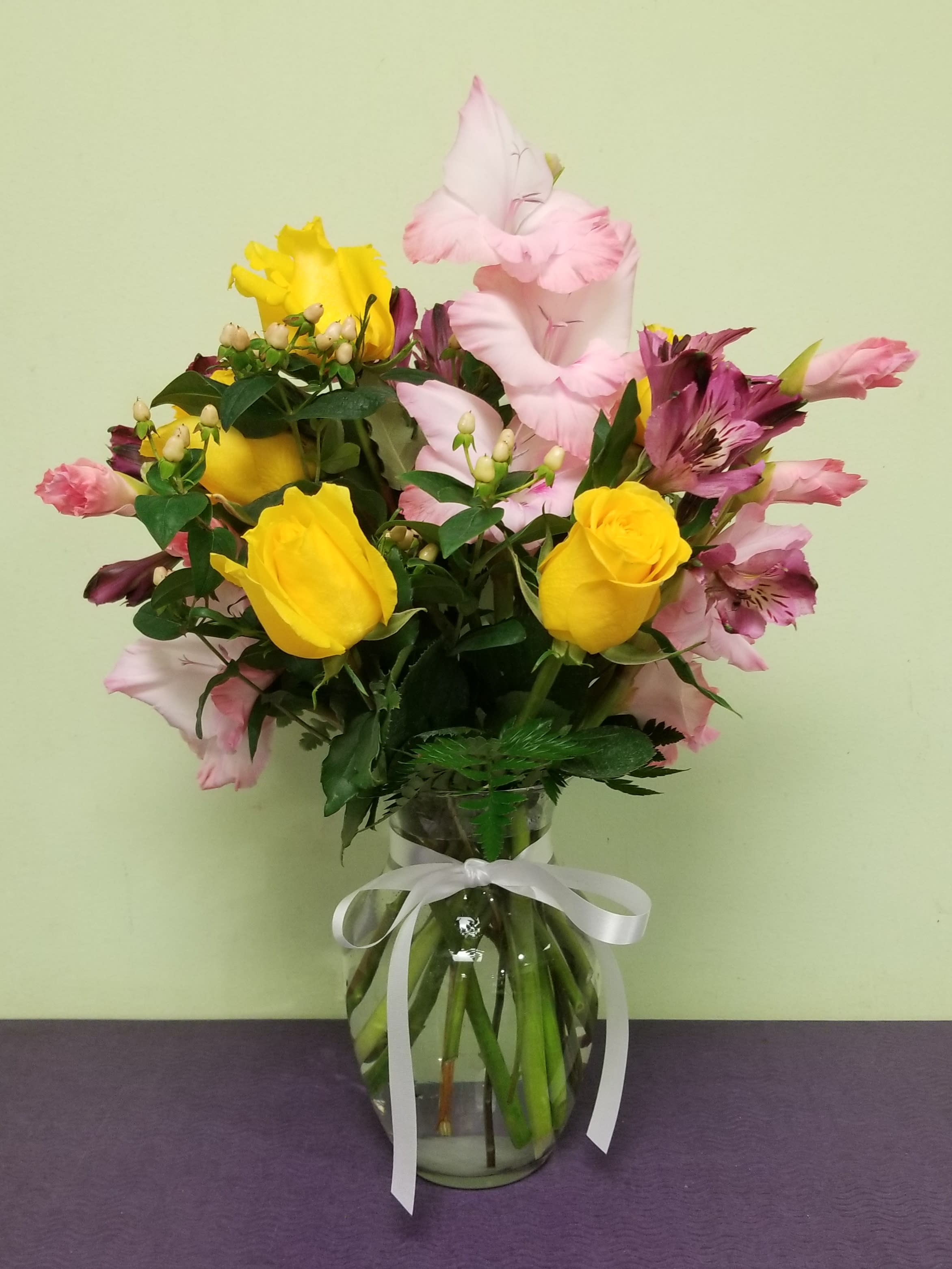 Bouquet of yellow roses and pink alstroemeria in a glass vase with a white ribbon