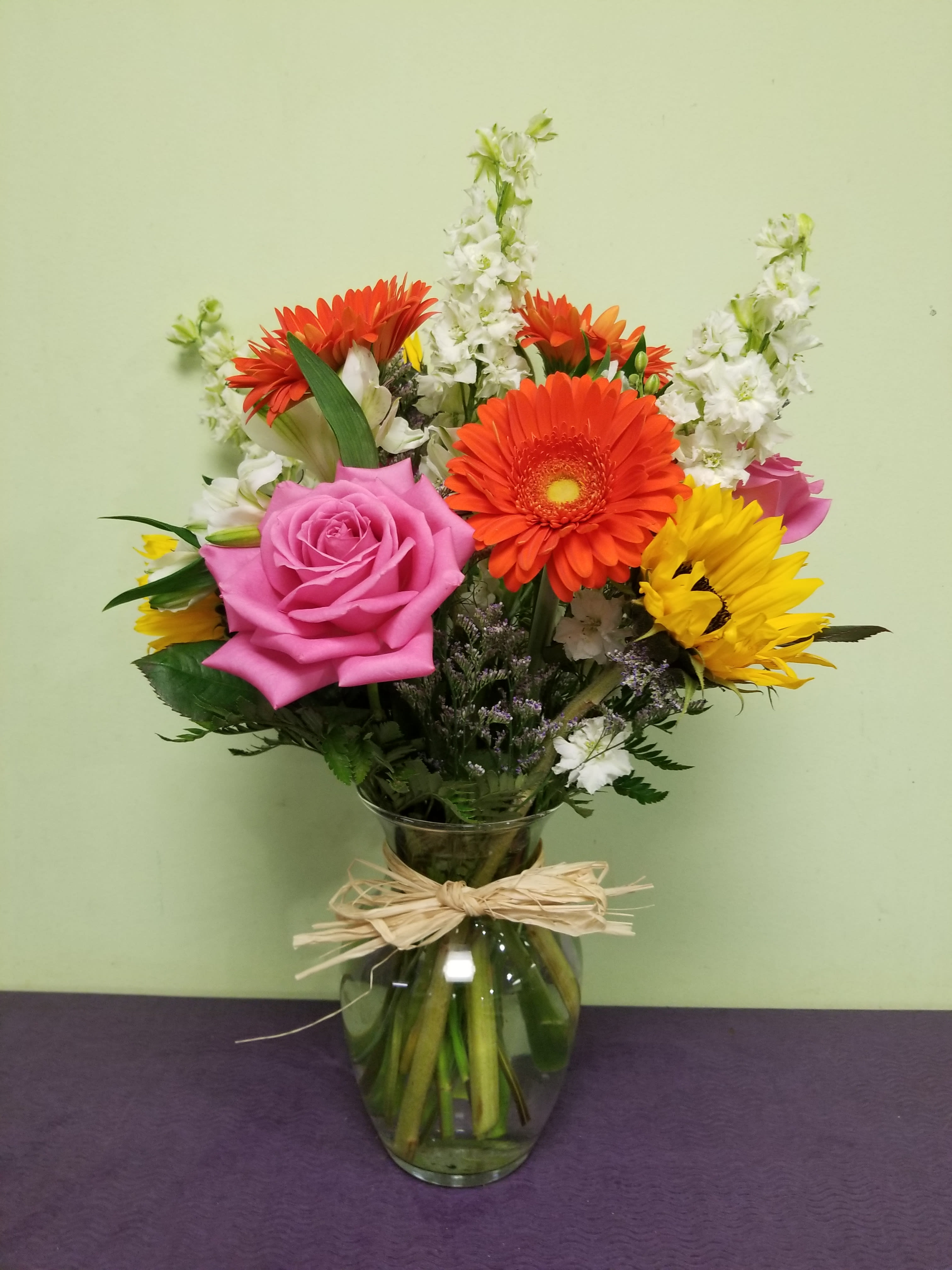 Mixed bouquet of pink, orange, and yellow flowers in a glass vase