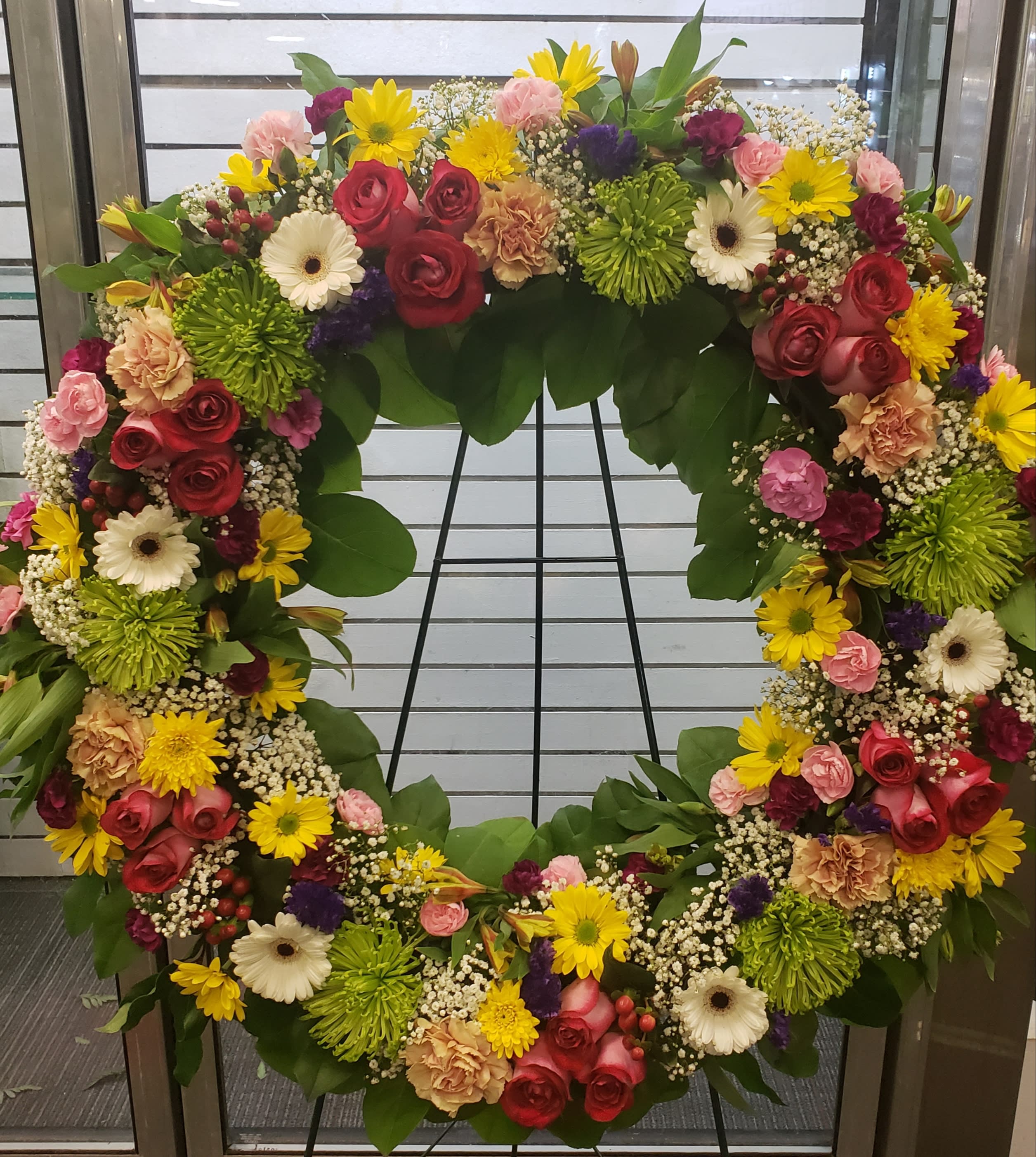Large circular floral wreath with mixed roses, daisies, and mums