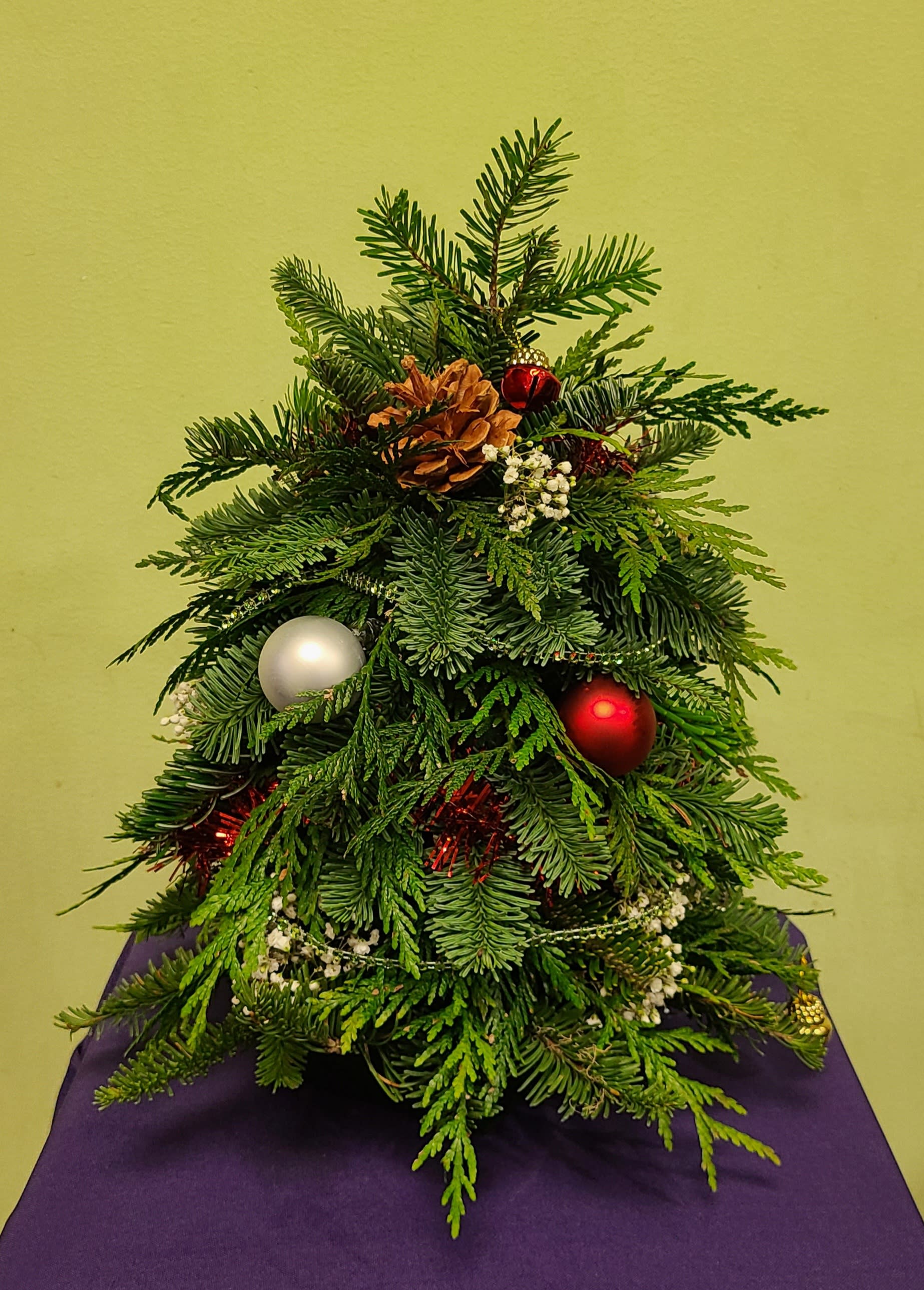Small evergreen arrangement decorated with ornaments and a pinecone