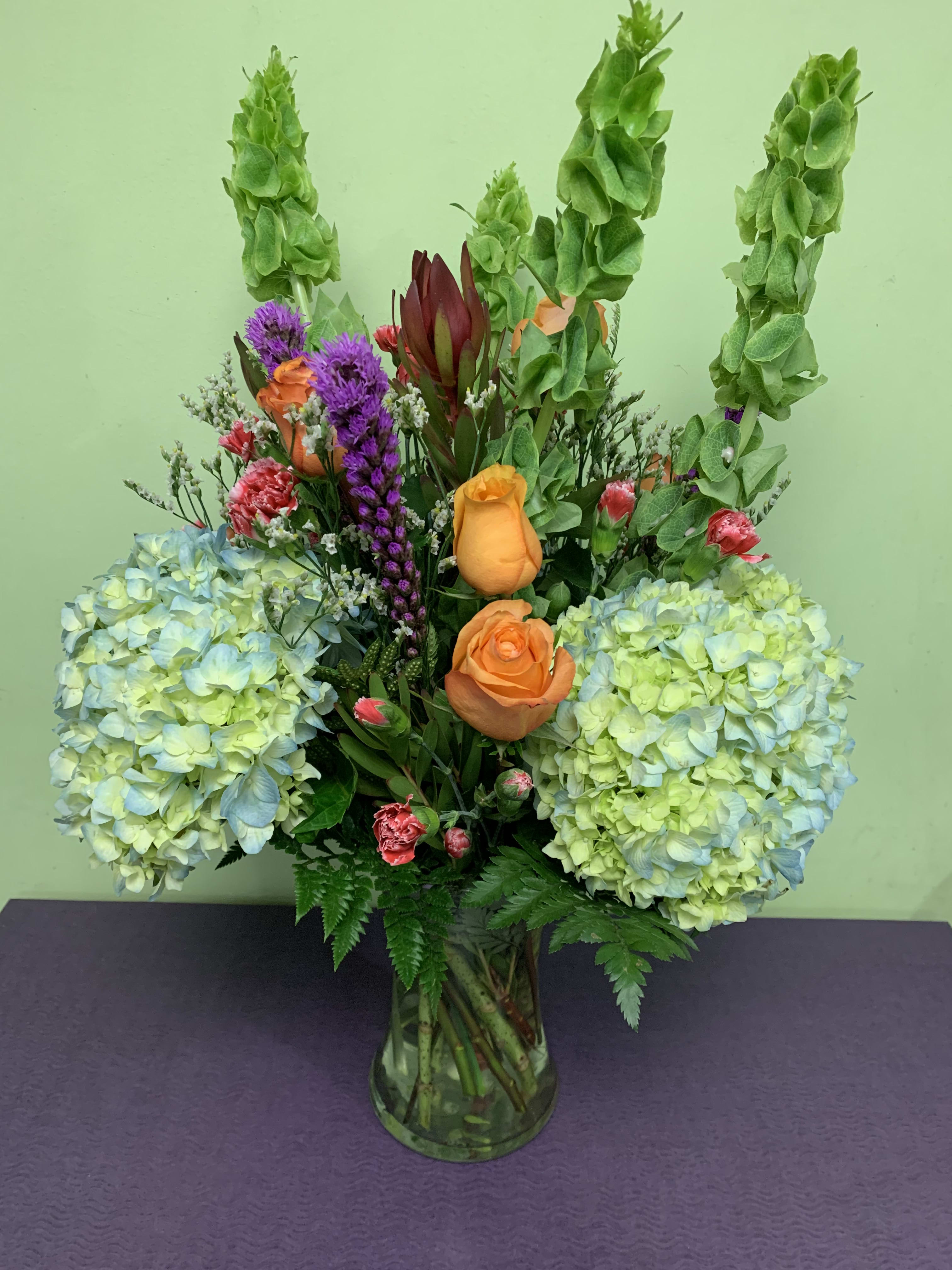 Mixed bouquet in a glass vase with hydrangeas, roses, and tall green spikes