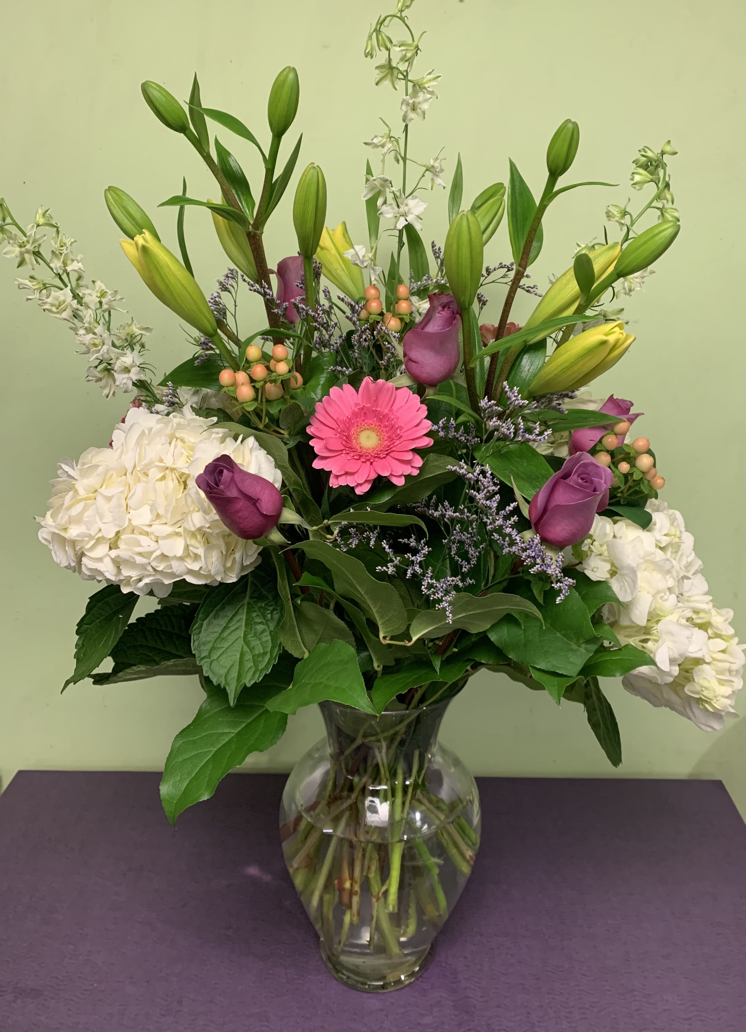 Mixed bouquet with lilies, roses, hydrangeas, and a pink gerbera in a glass vase