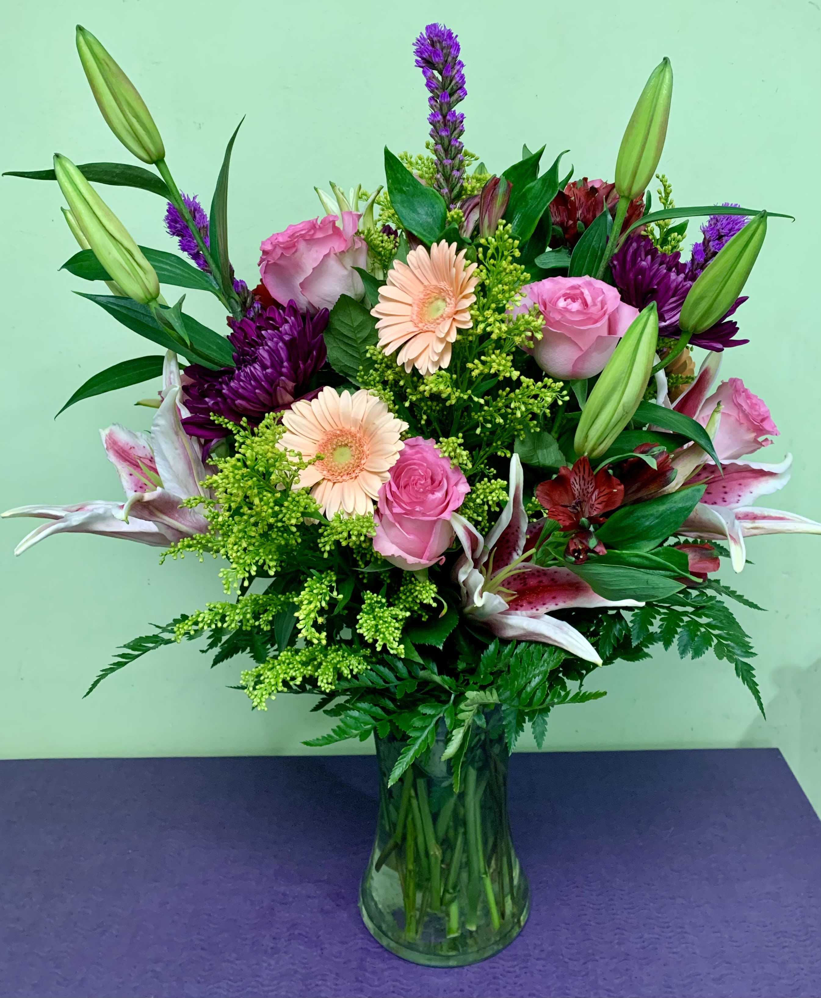 Mixed bouquet of pink roses, lilies, and purple flowers in a glass vase