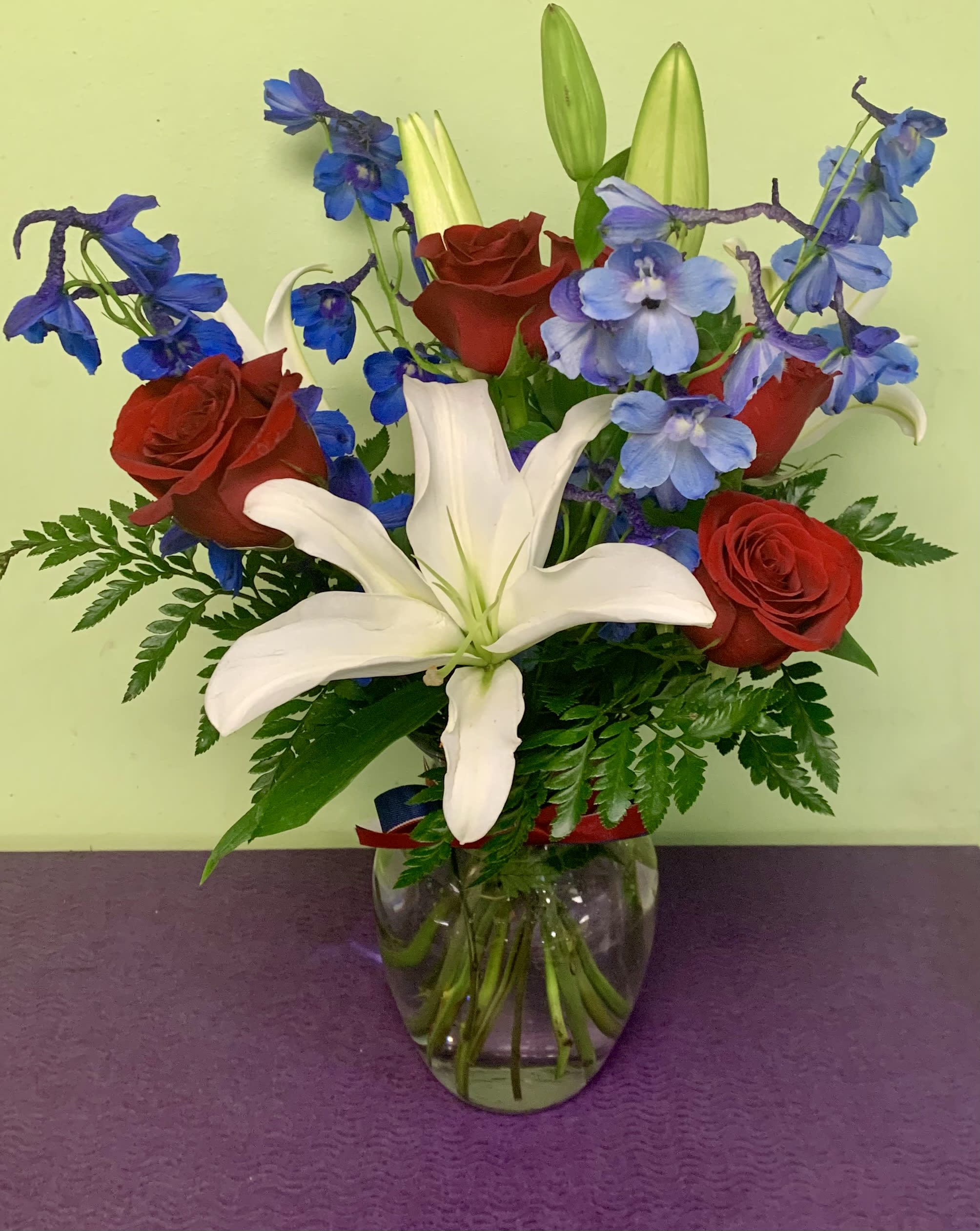 Bouquet of red roses, white lilies, and blue flowers in a glass vase