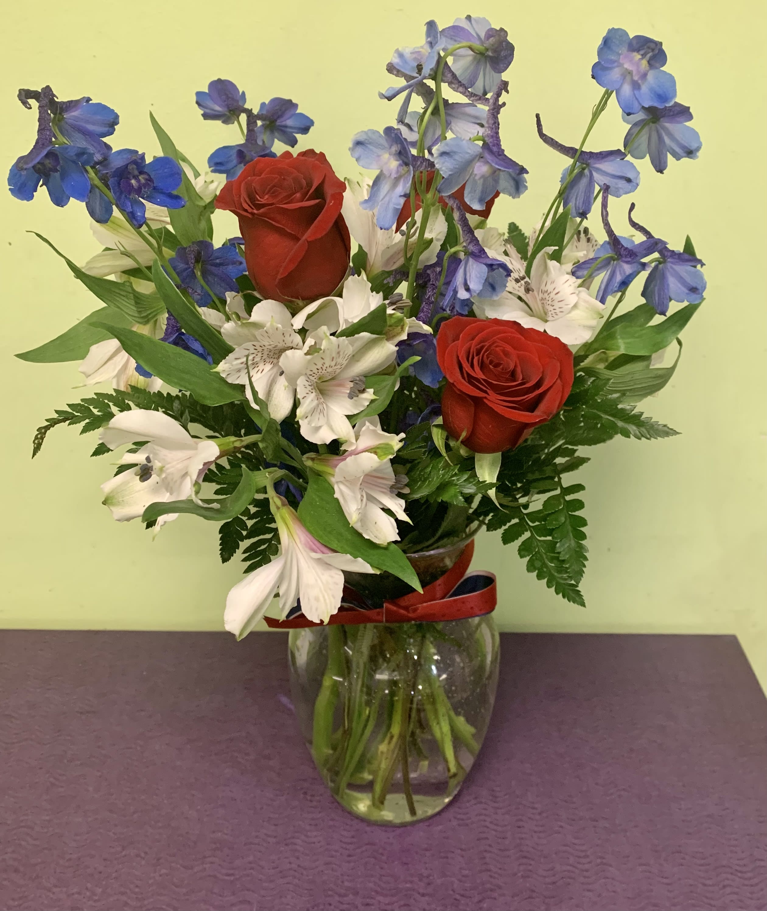 Bouquet of red roses, white alstroemeria, and blue delphinium in a glass vase