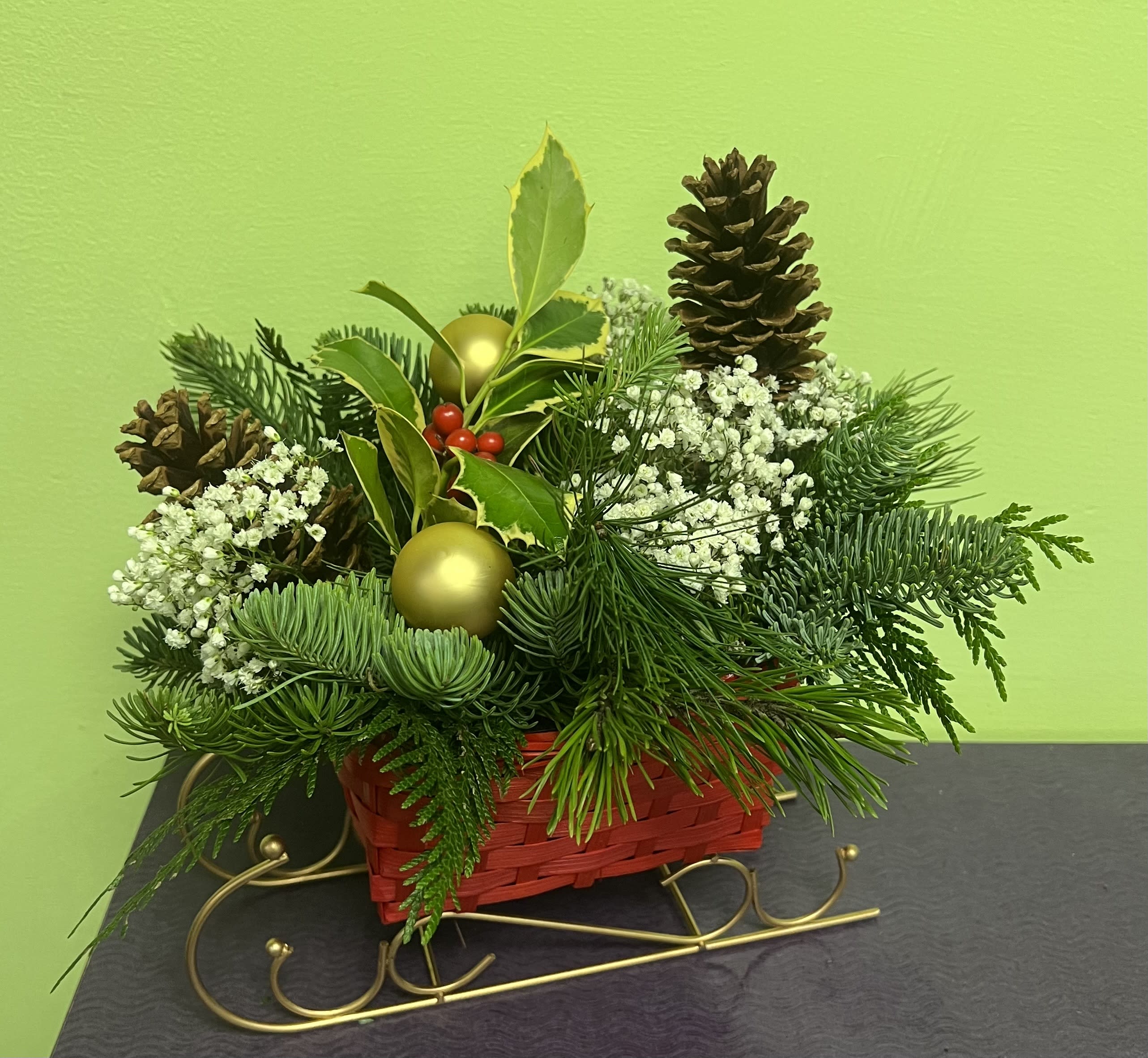 Holiday arrangement in a red basket with pinecones, white filler flowers, and gold ornaments