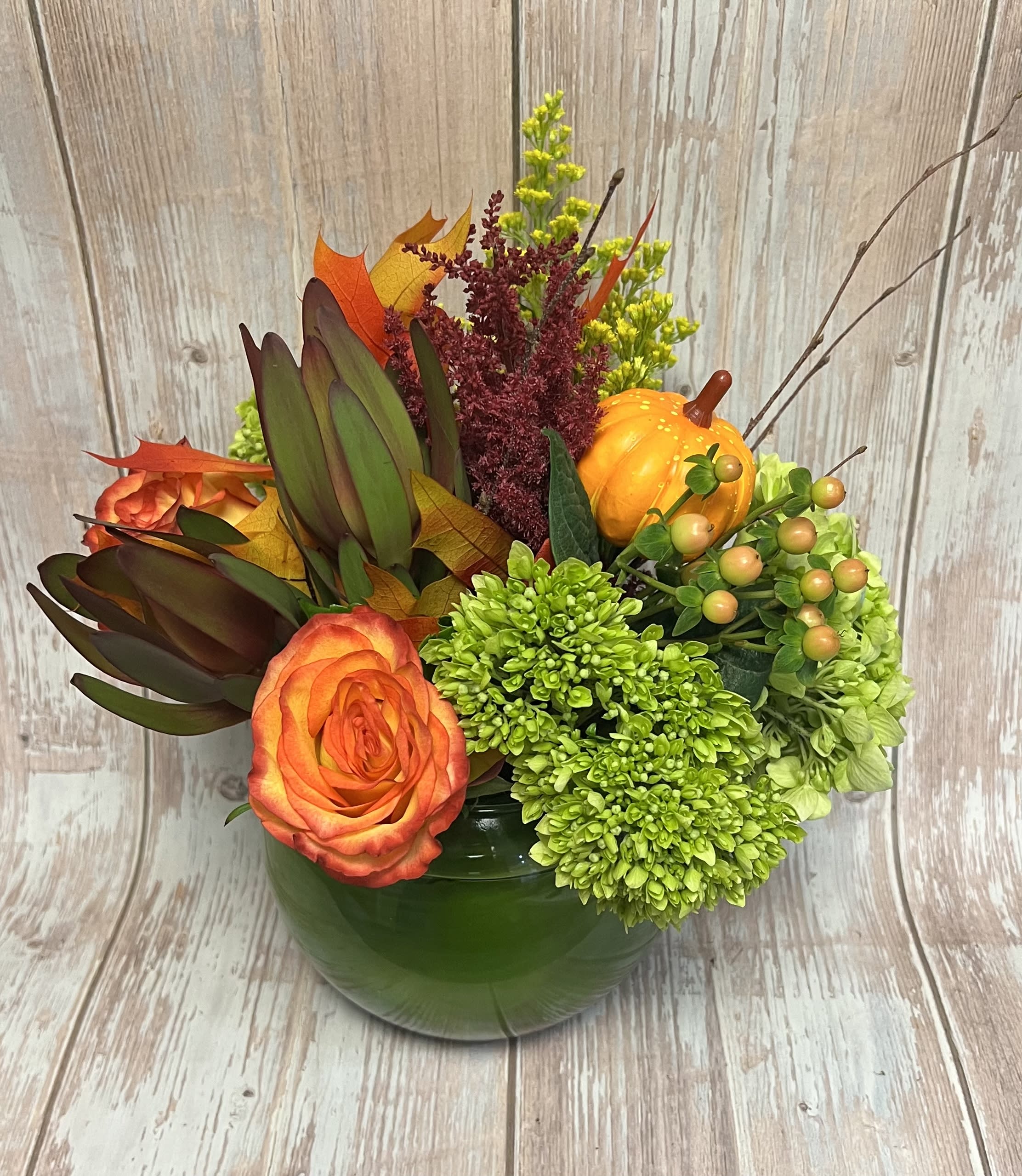 Orange rose arrangement in a green vase with pumpkins and autumn foliage