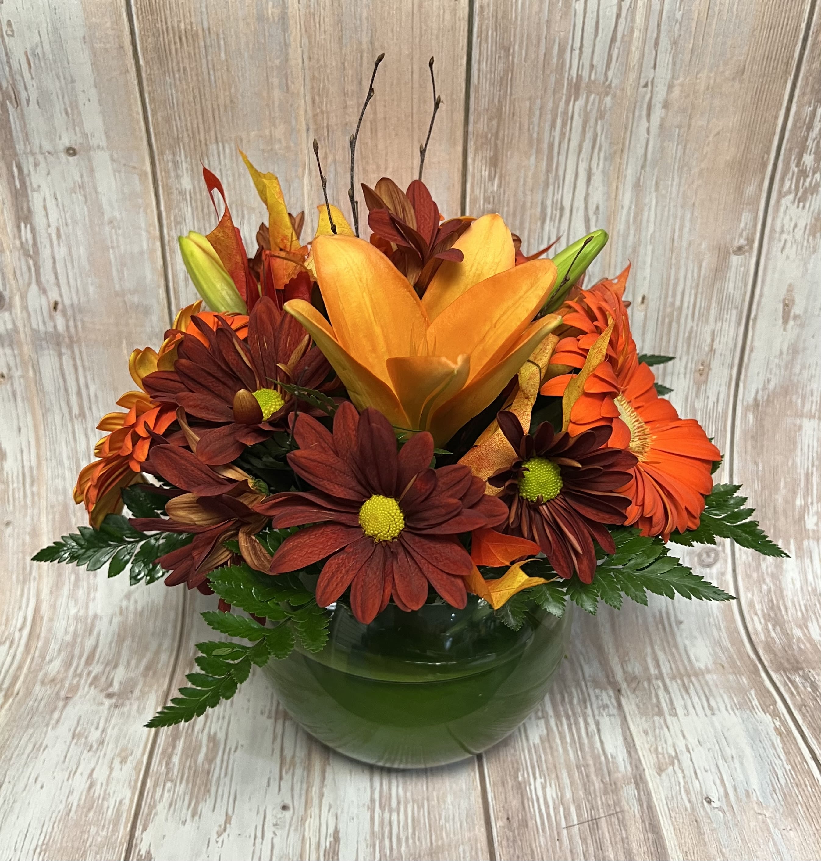 Orange and burgundy floral arrangement in a green glass vase