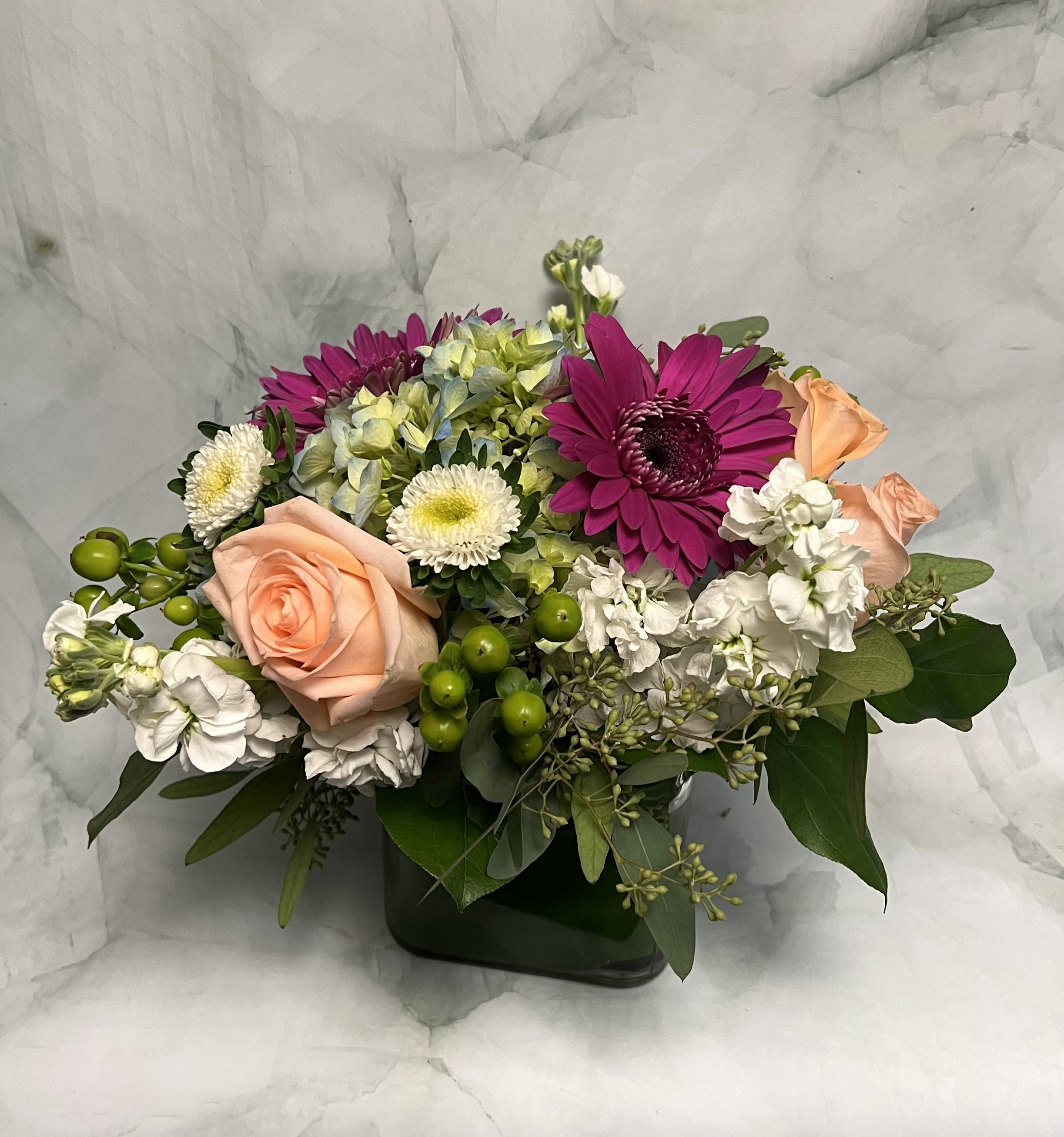 Mixed bouquet with peach roses, magenta daisies, and white blooms in a dark vase