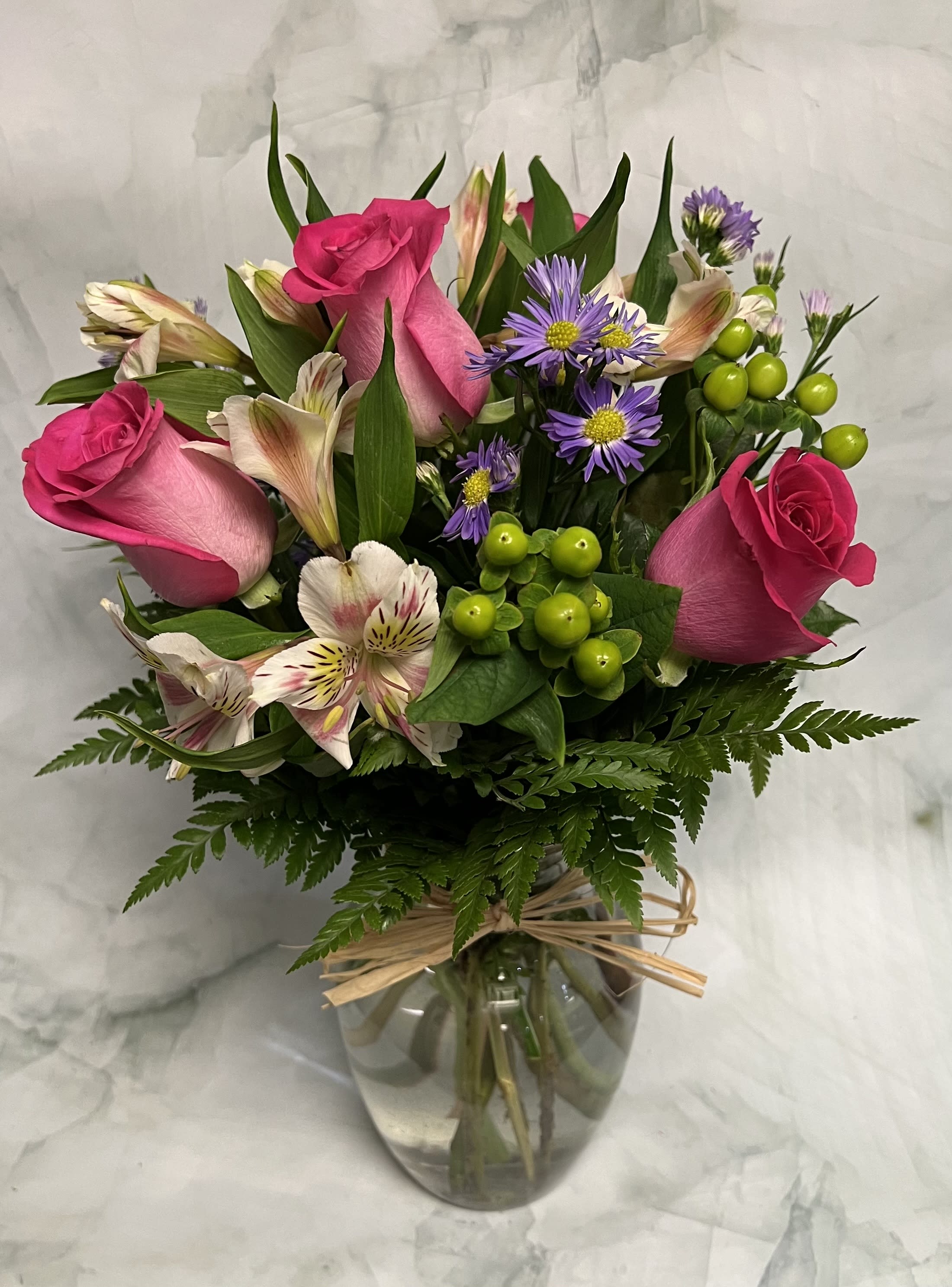 Pink roses and purple daisies arranged in a glass vase