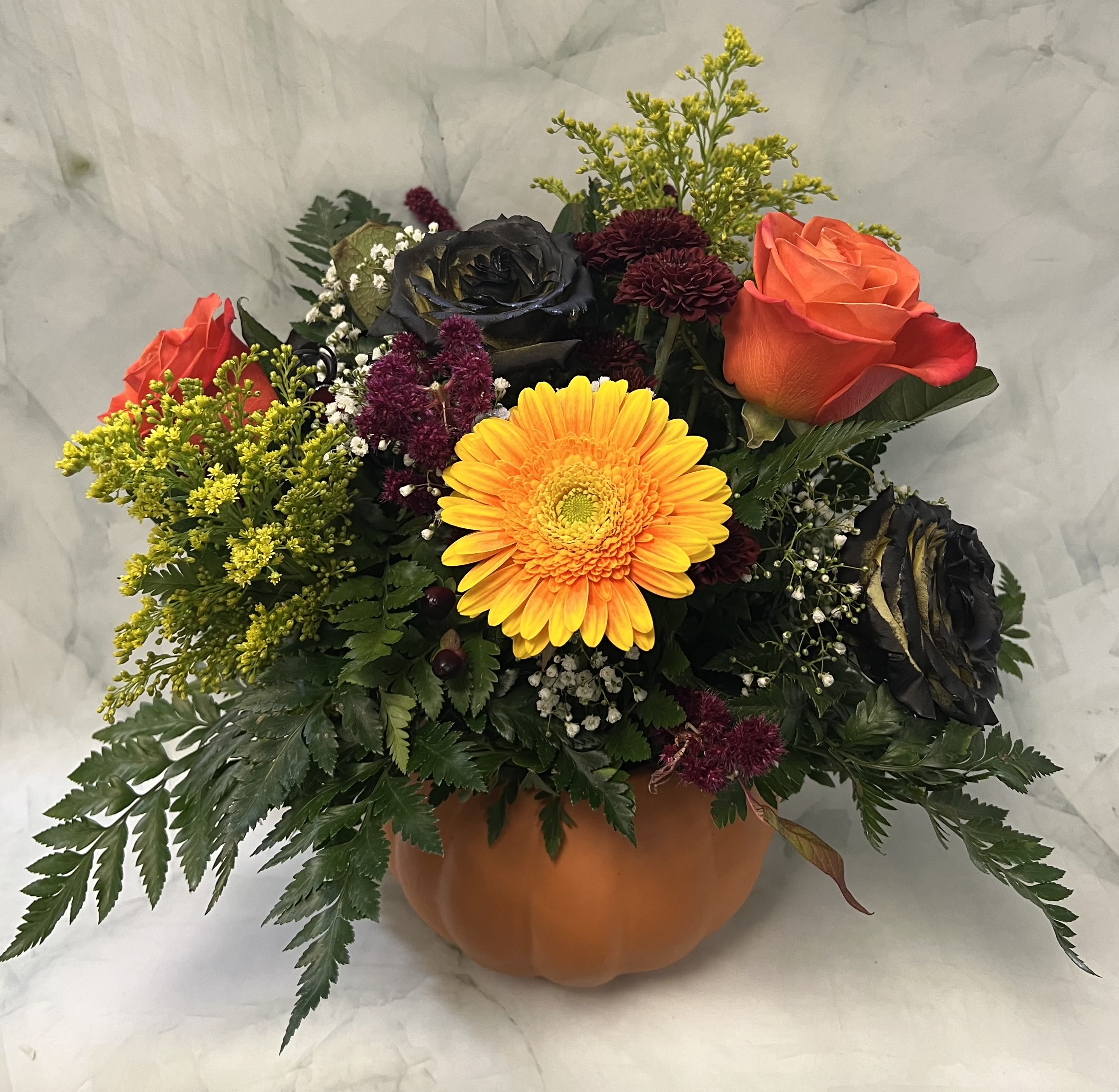 Autumn floral arrangement in a pumpkin-shaped container with roses and a yellow gerbera daisy