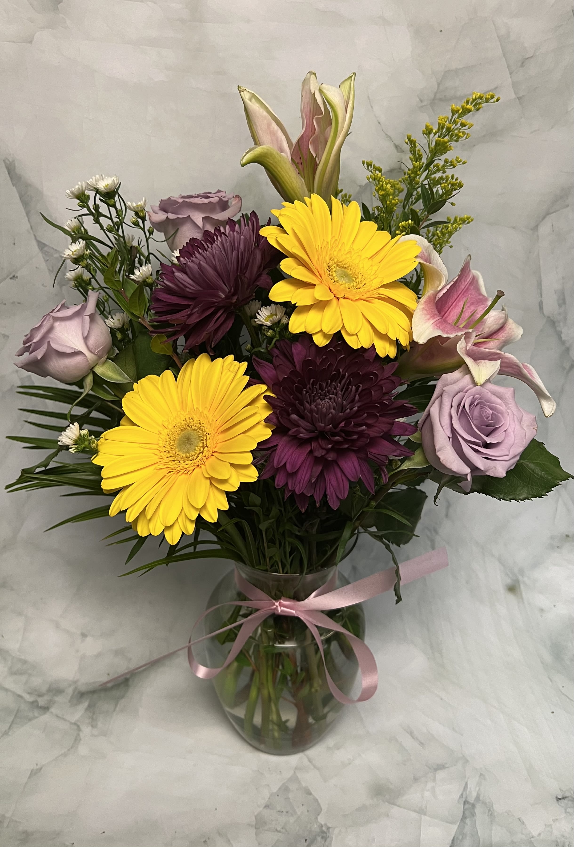 Bouquet of yellow gerbera daisies, purple chrysanthemums, and lavender roses in a glass vase