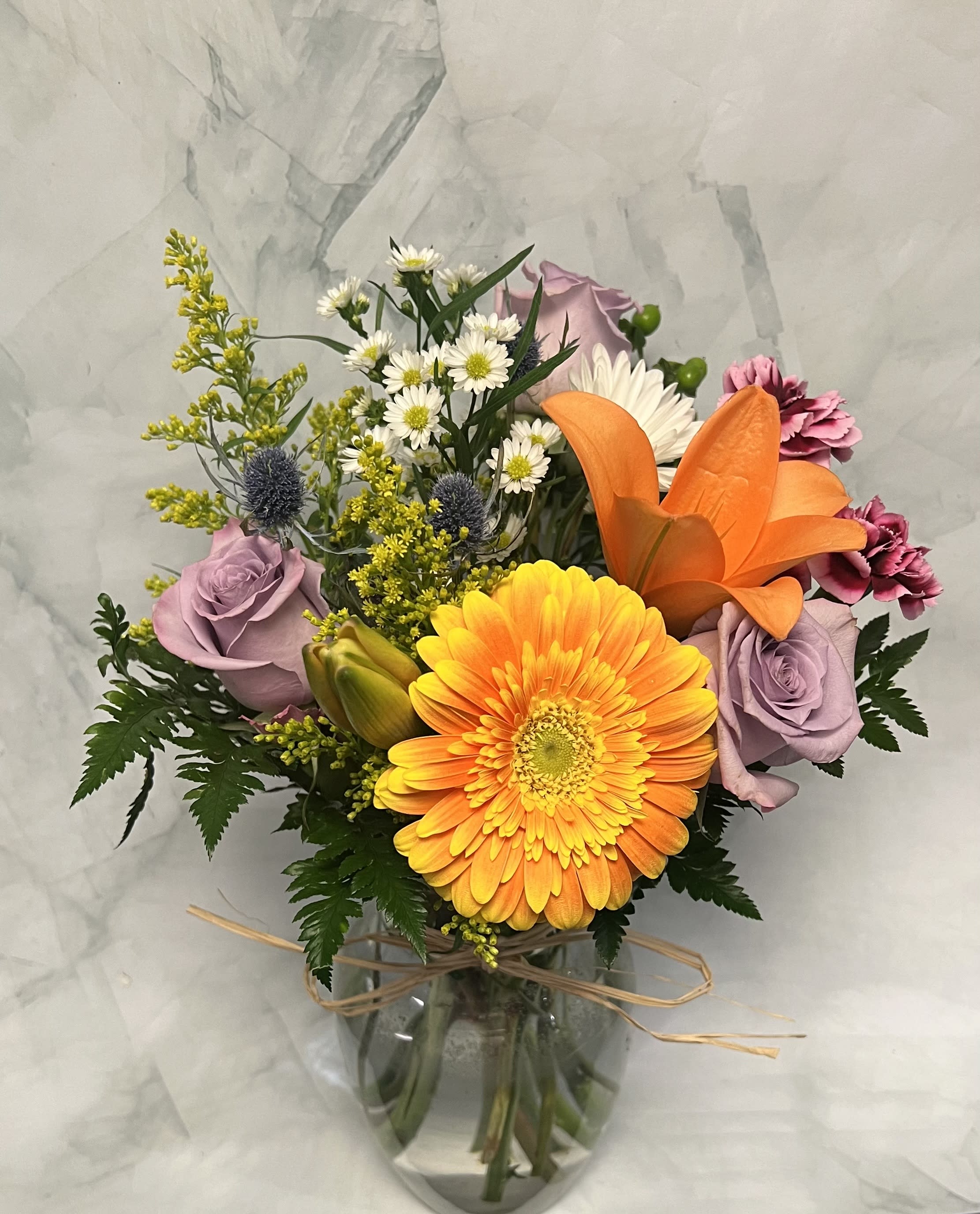Mixed bouquet with orange gerbera, lavender roses, and lilies in a glass vase