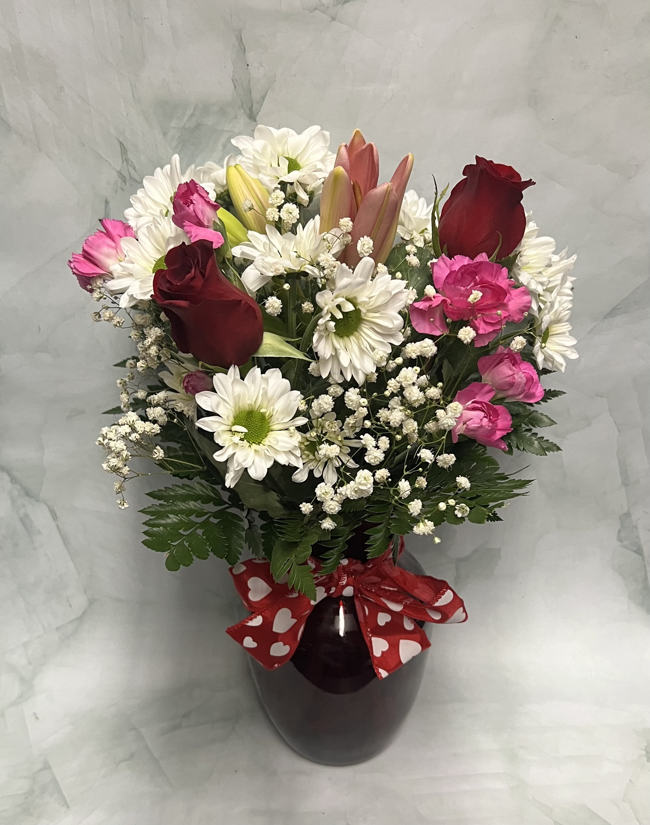 Bouquet of red roses, pink carnations, and white daisies in a dark vase