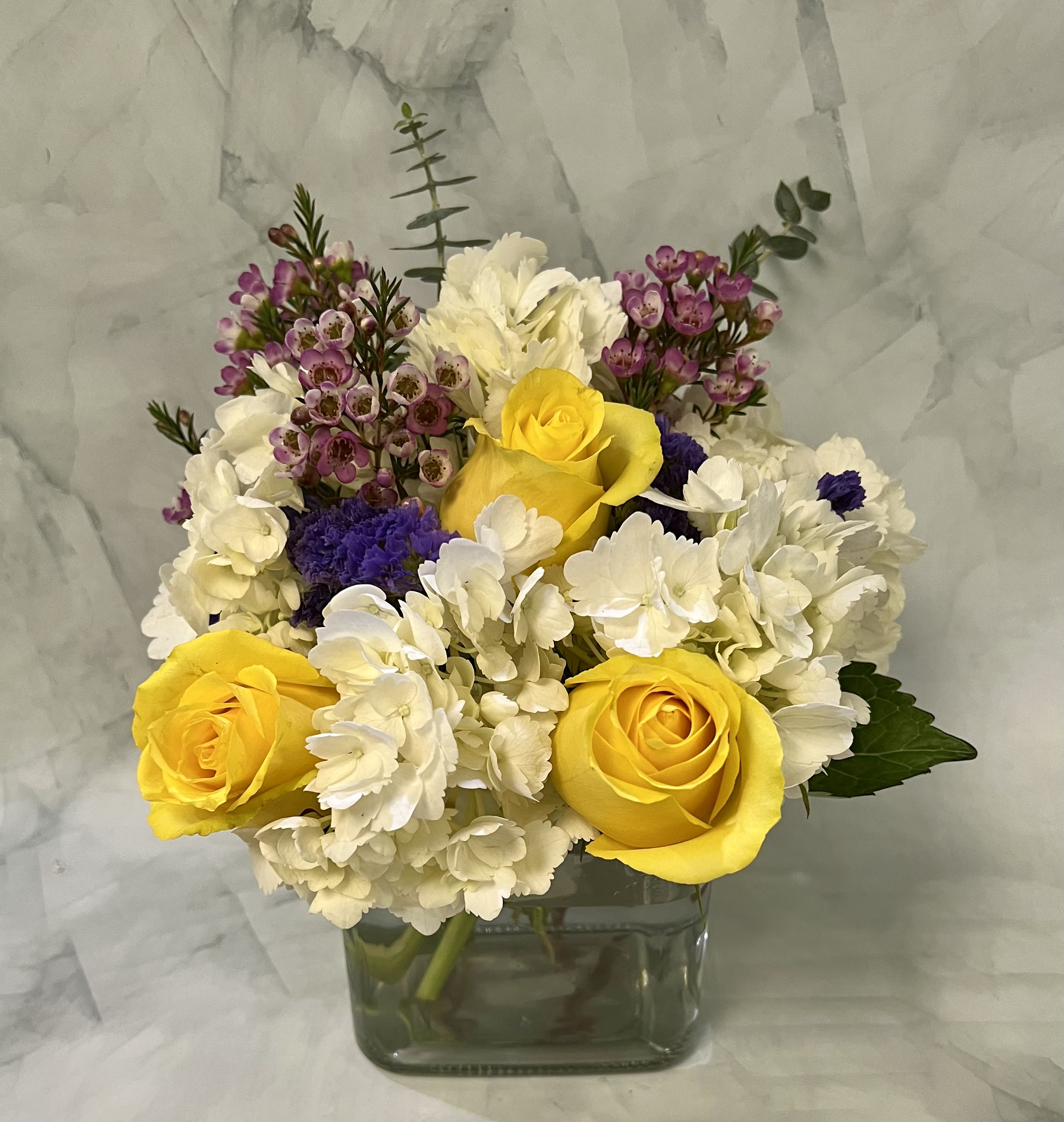 Yellow roses and white hydrangeas in a square glass vase