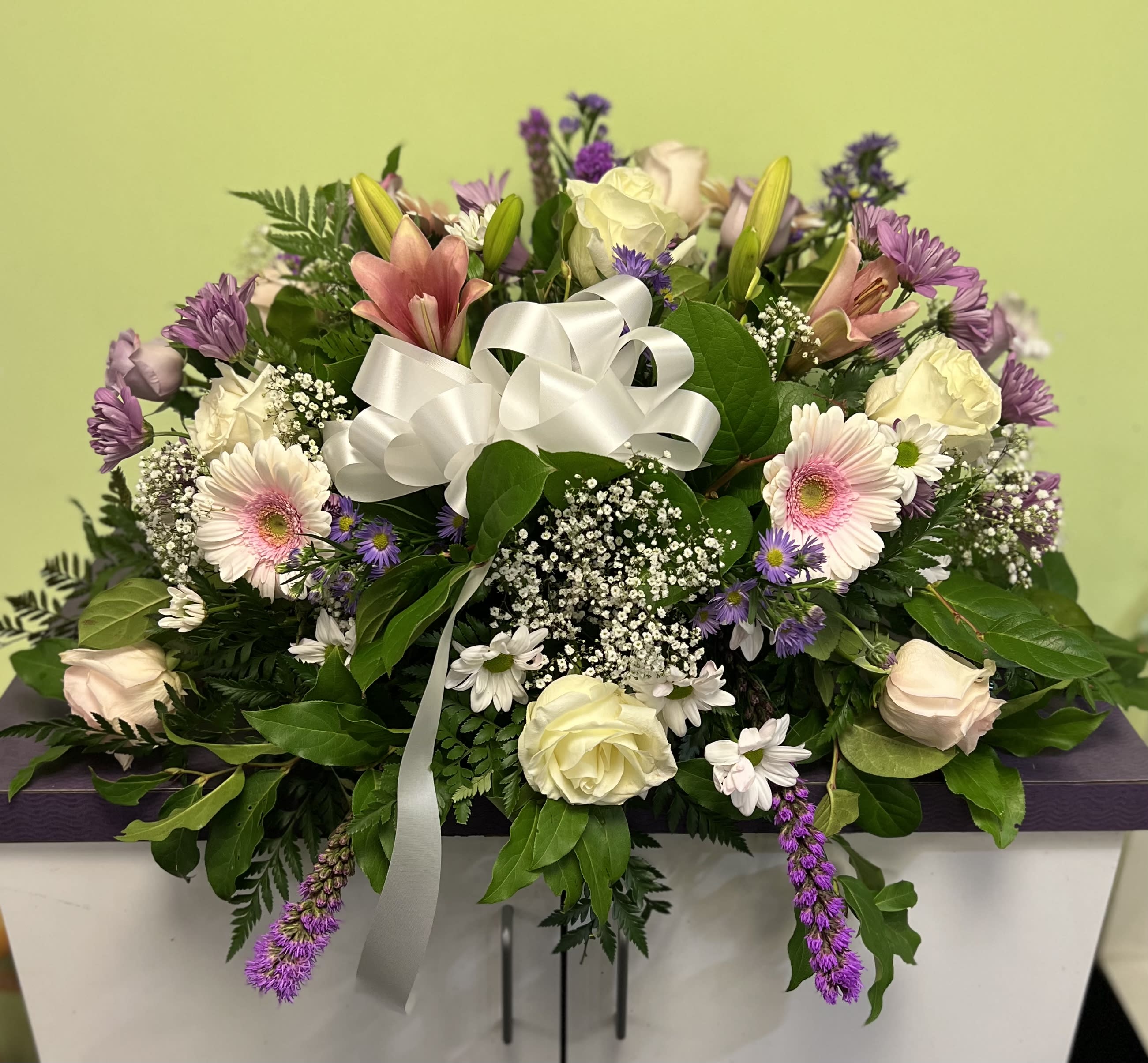 Mixed bouquet with pink lilies, roses, and purple flowers tied with a white ribbon