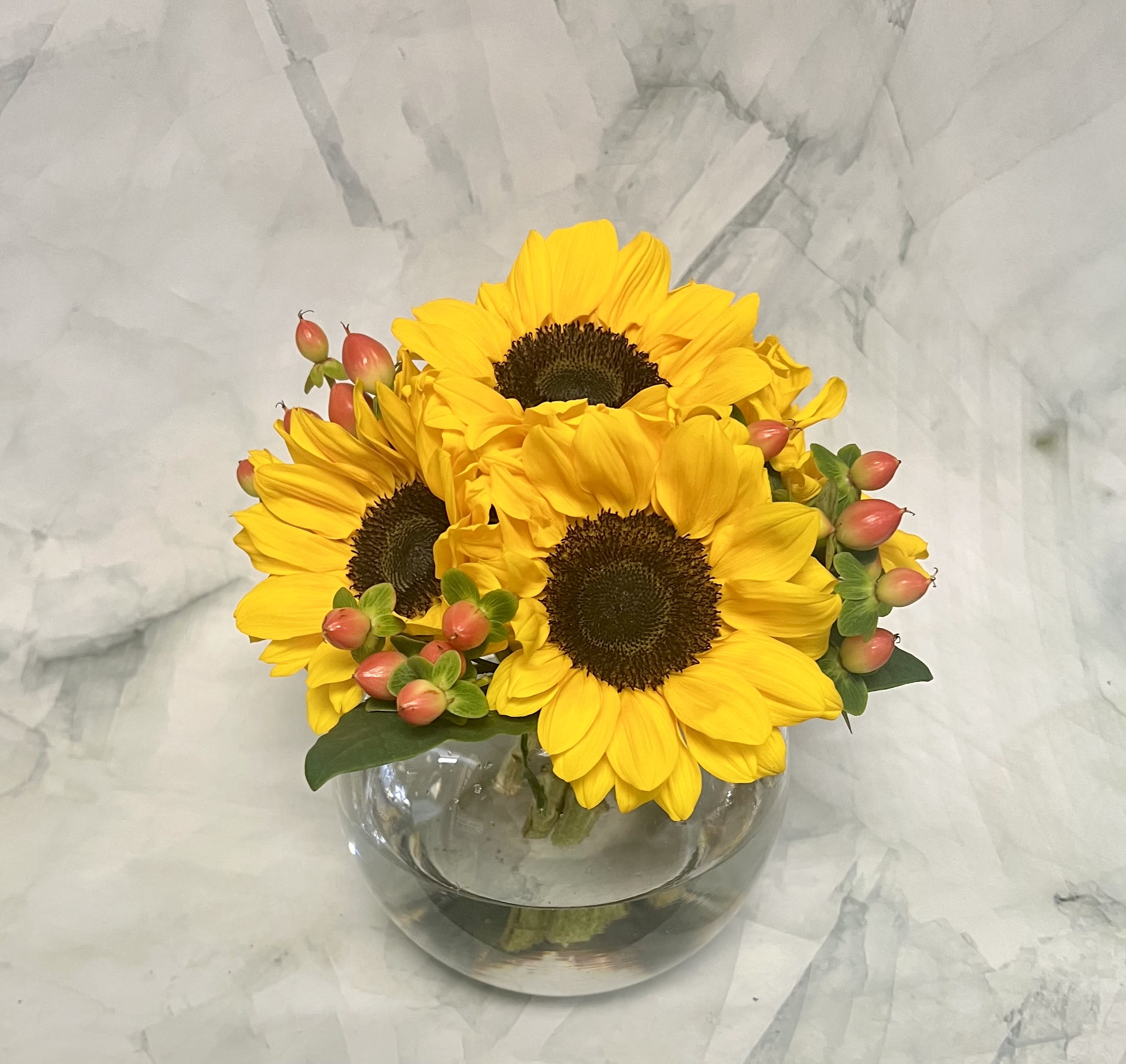 Yellow sunflowers in a round glass vase with pink berry accents