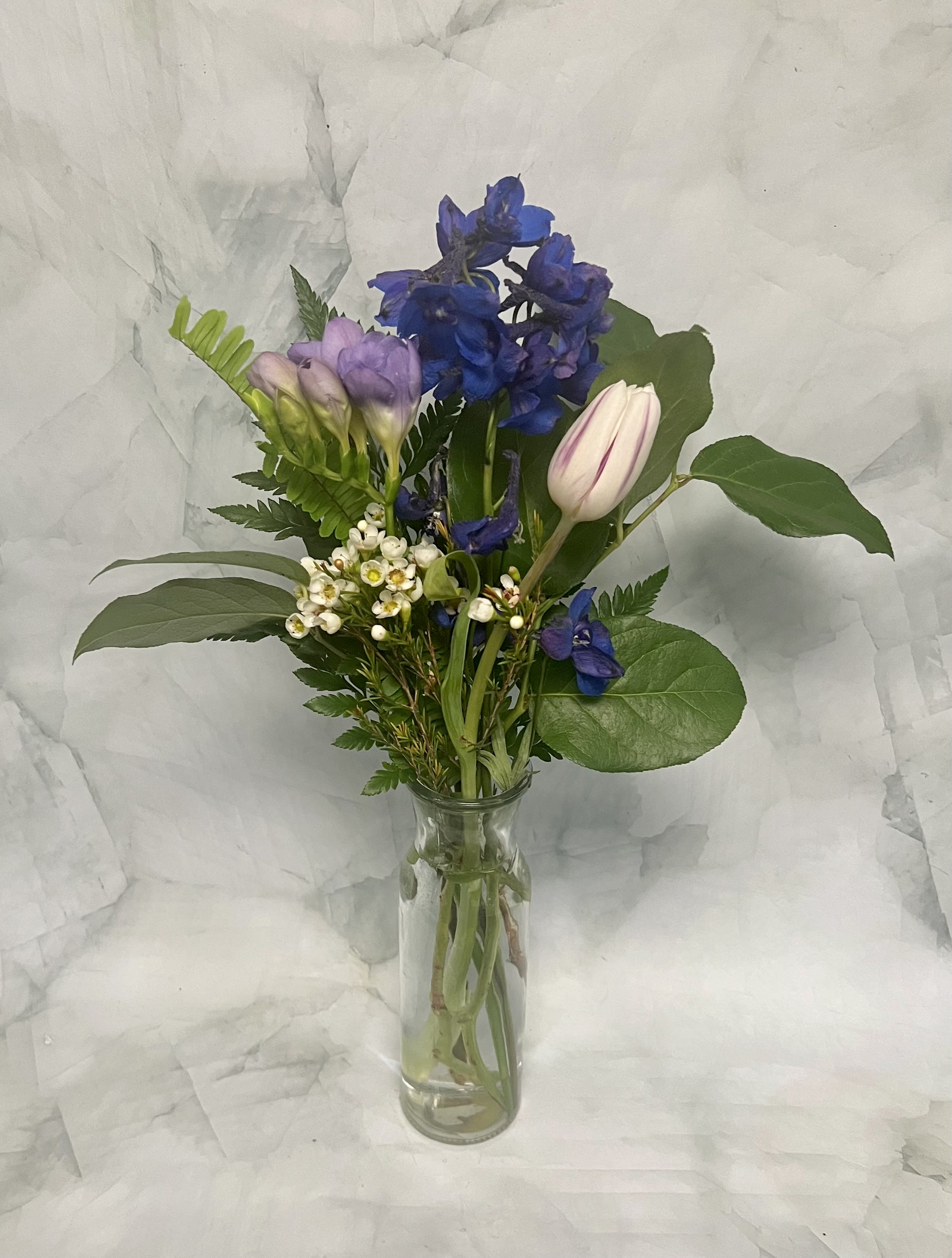 Mixed bouquet of blue, lavender, and white flowers in a clear glass vase