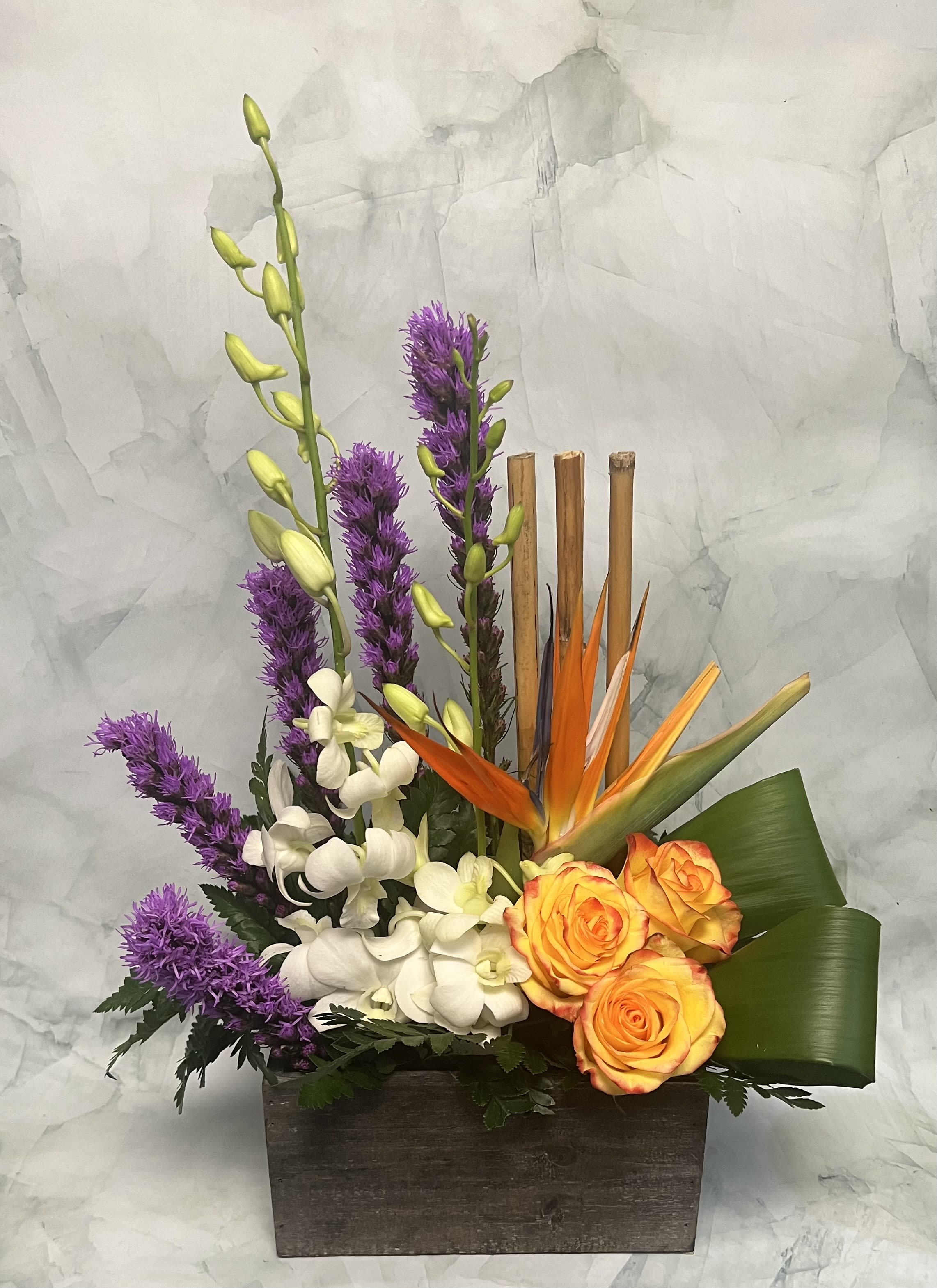 Tropical floral arrangement with orange roses, white orchids, and purple spikes in a wooden box