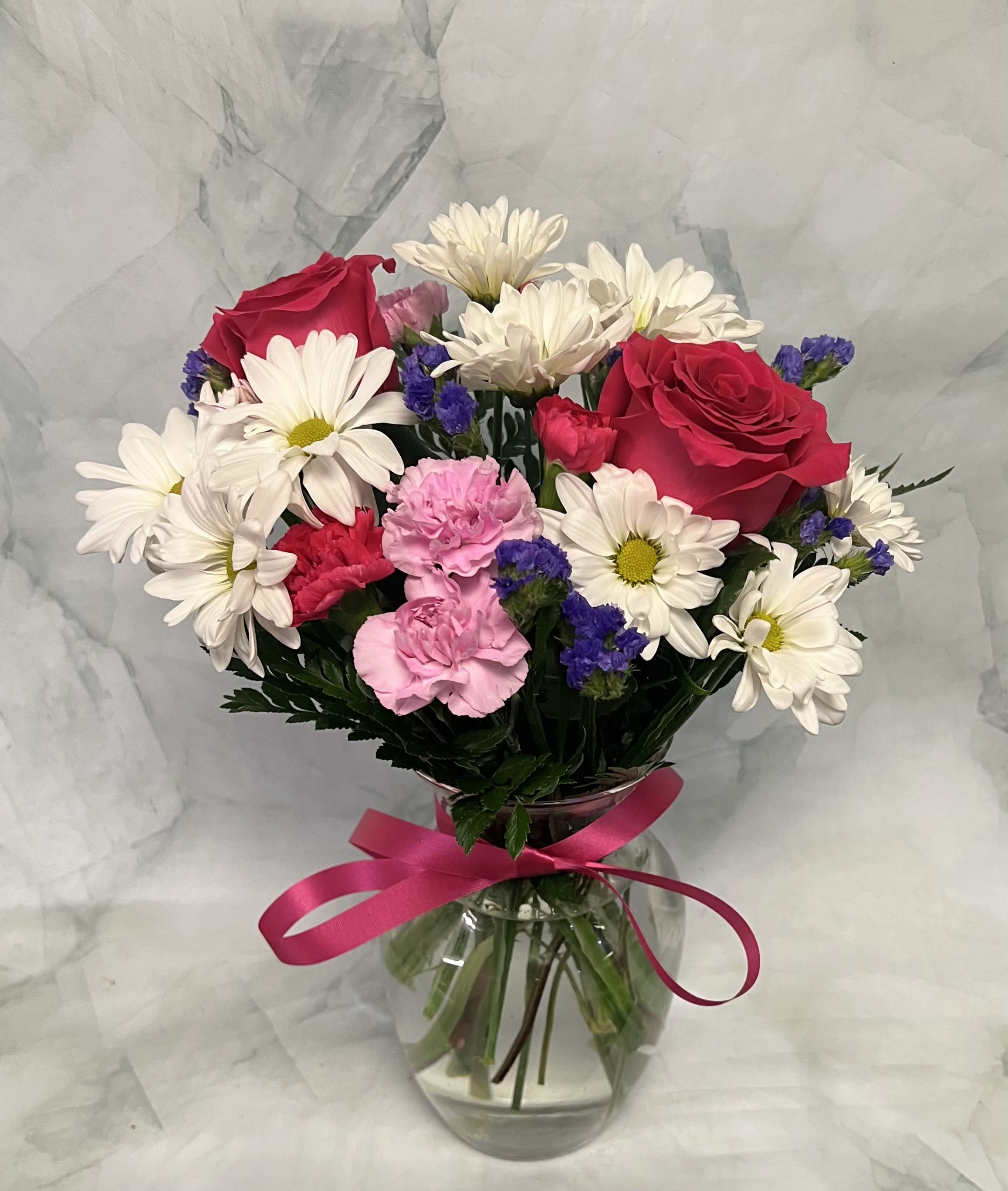 Bouquet of red roses, white daisies, and pink carnations in a glass vase