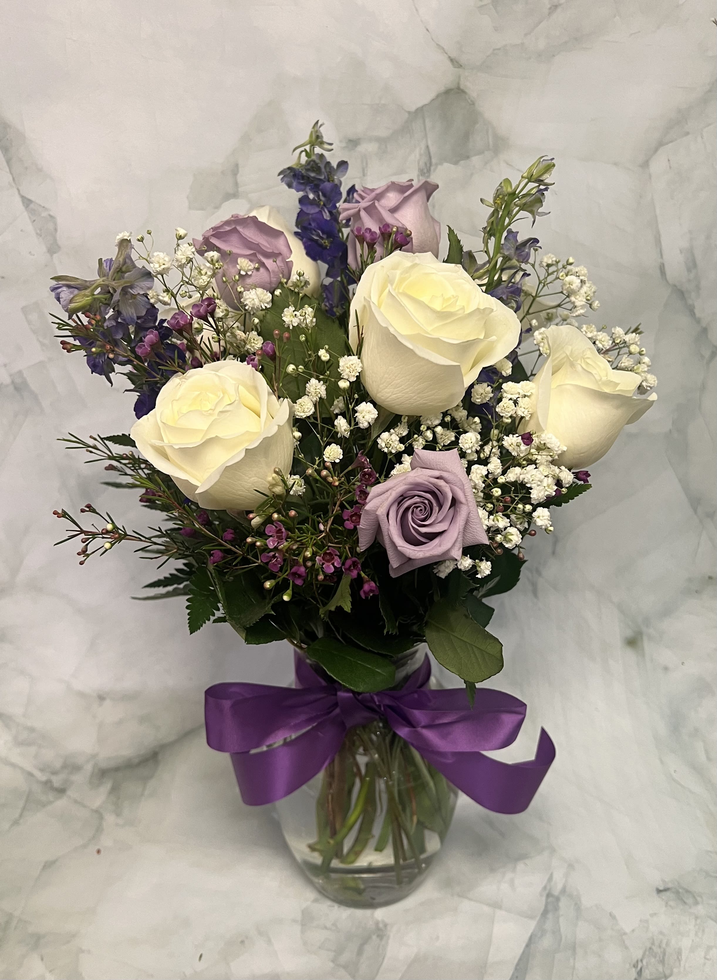 Bouquet of cream and lavender roses in a glass vase with a purple ribbon