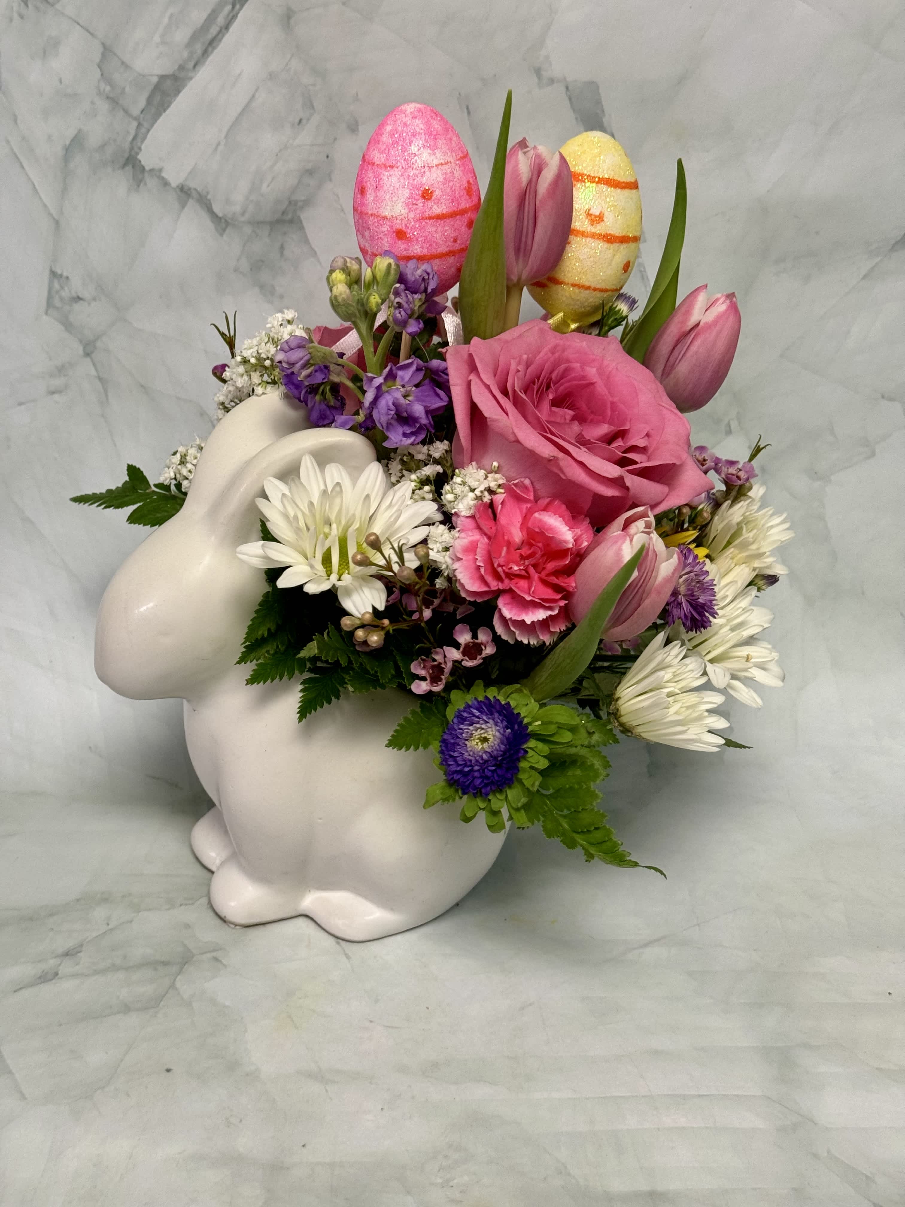Pink and white floral arrangement in a white bunny container with decorative eggs