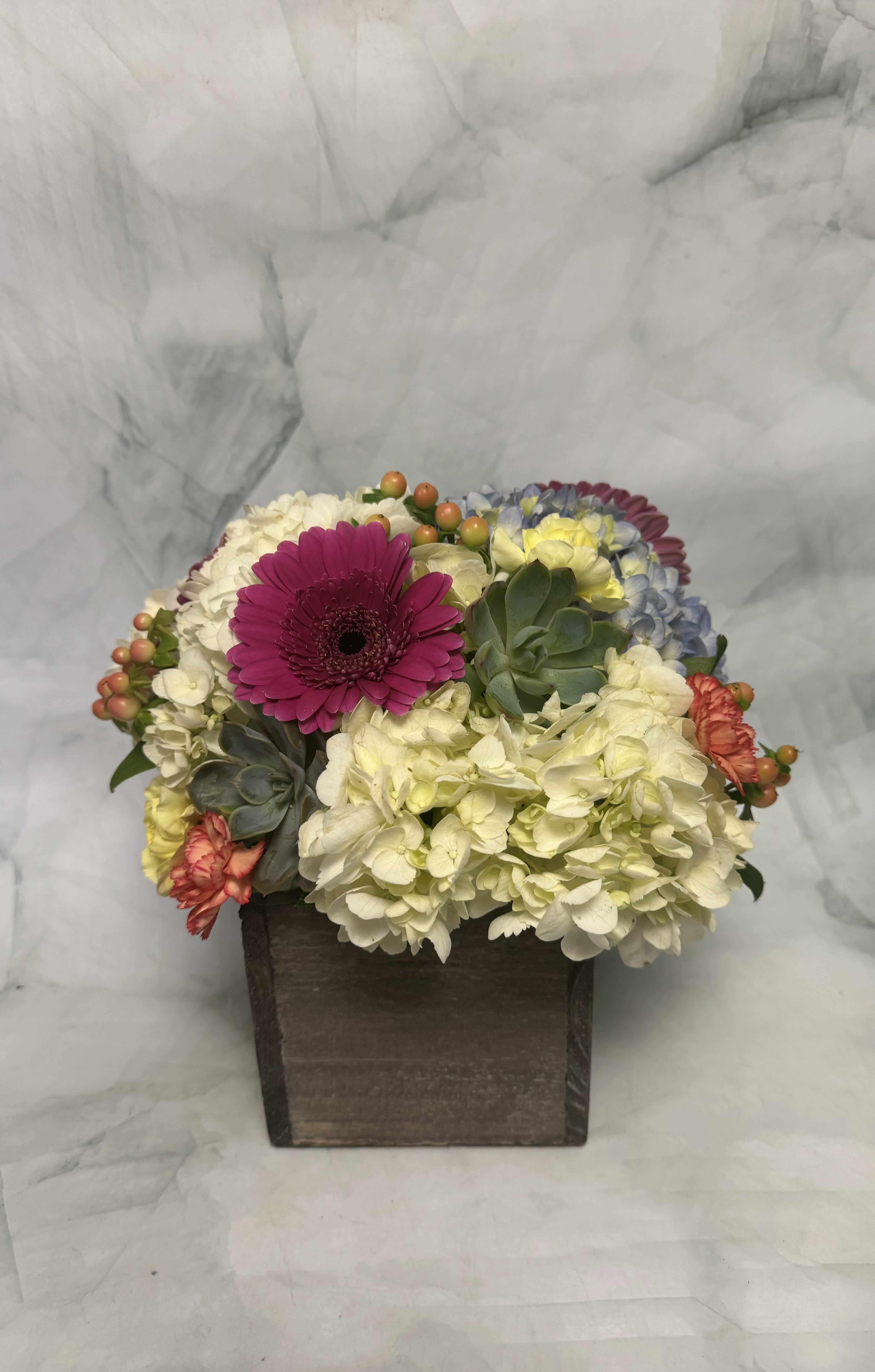 Mixed flowers in a dark wooden box with a bright pink daisy-like bloom